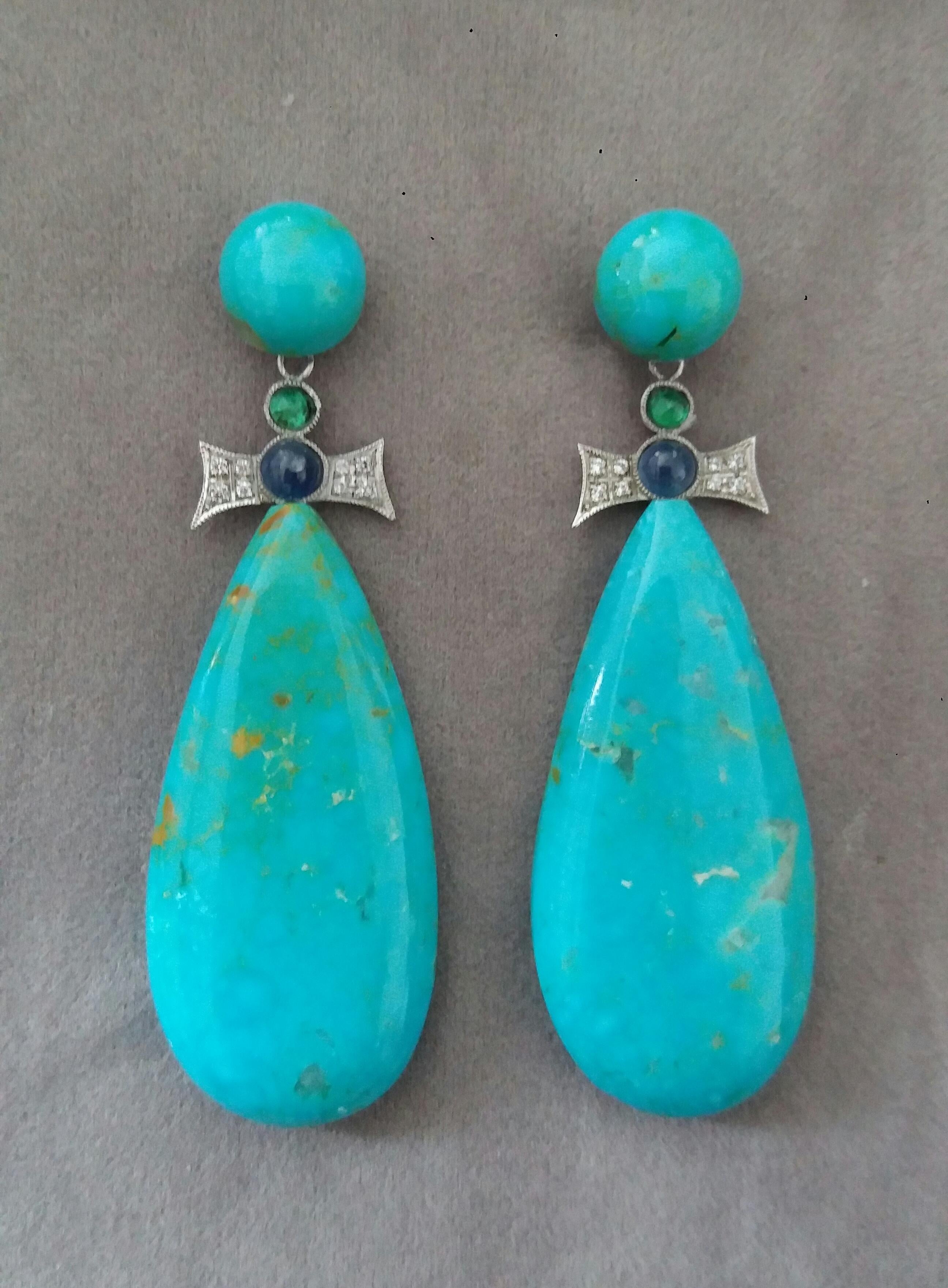 In these Art Deco Style handmade earrings 2 good quality Natural Turquoise plain drops measuring 20 x 43 mm. are suspended from 2 bow shape 14 kt white gold elements with 16 full cut round Diamonds , Blue Sapphires and Emeralds small round