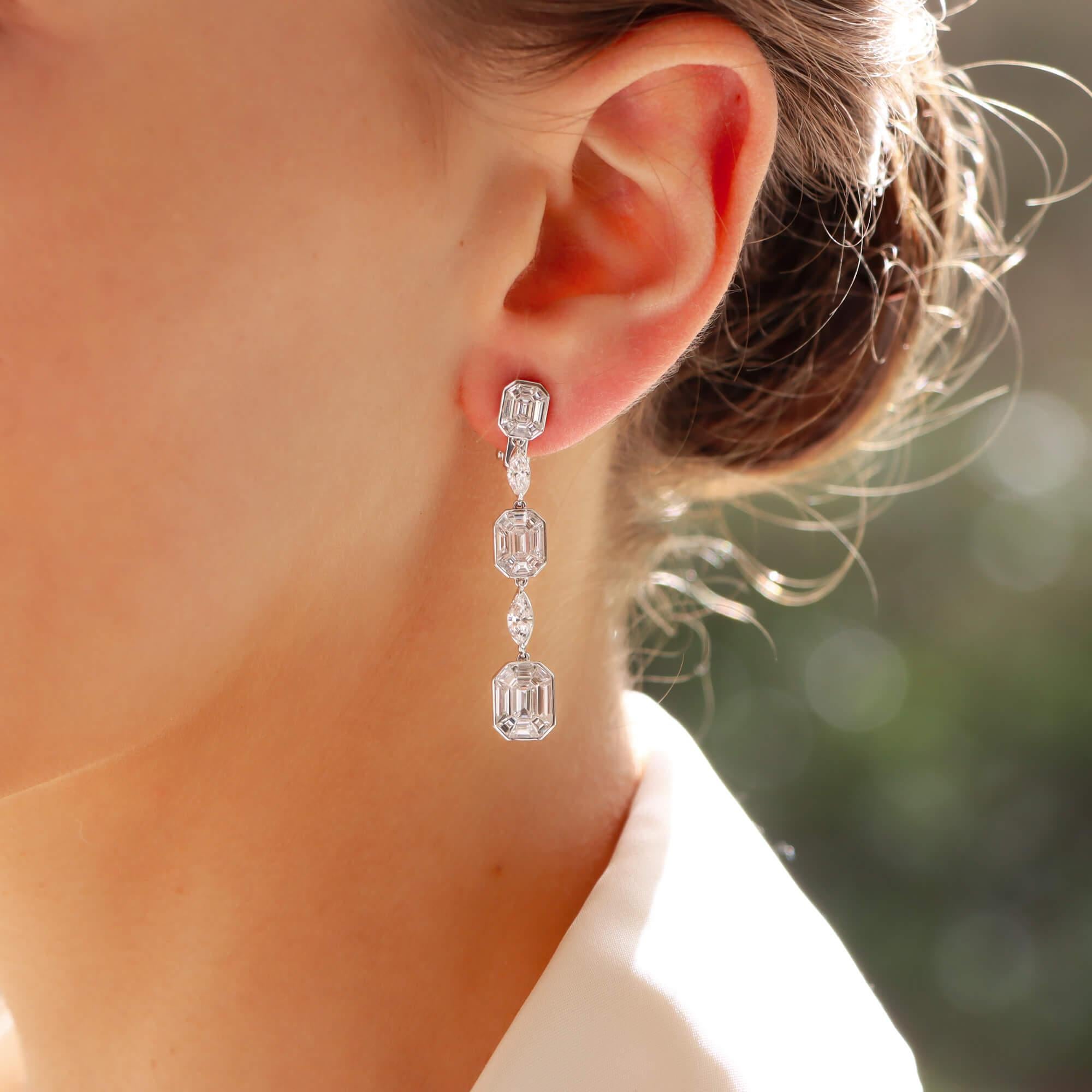 A stunning pair graduated emerald cut diamond cluster drop earrings in platinum.

Each earring consists of a total of 3 graduated emerald and baguette cut diamond cluster sections which are all rubover set and interspaced with a claw set marquise