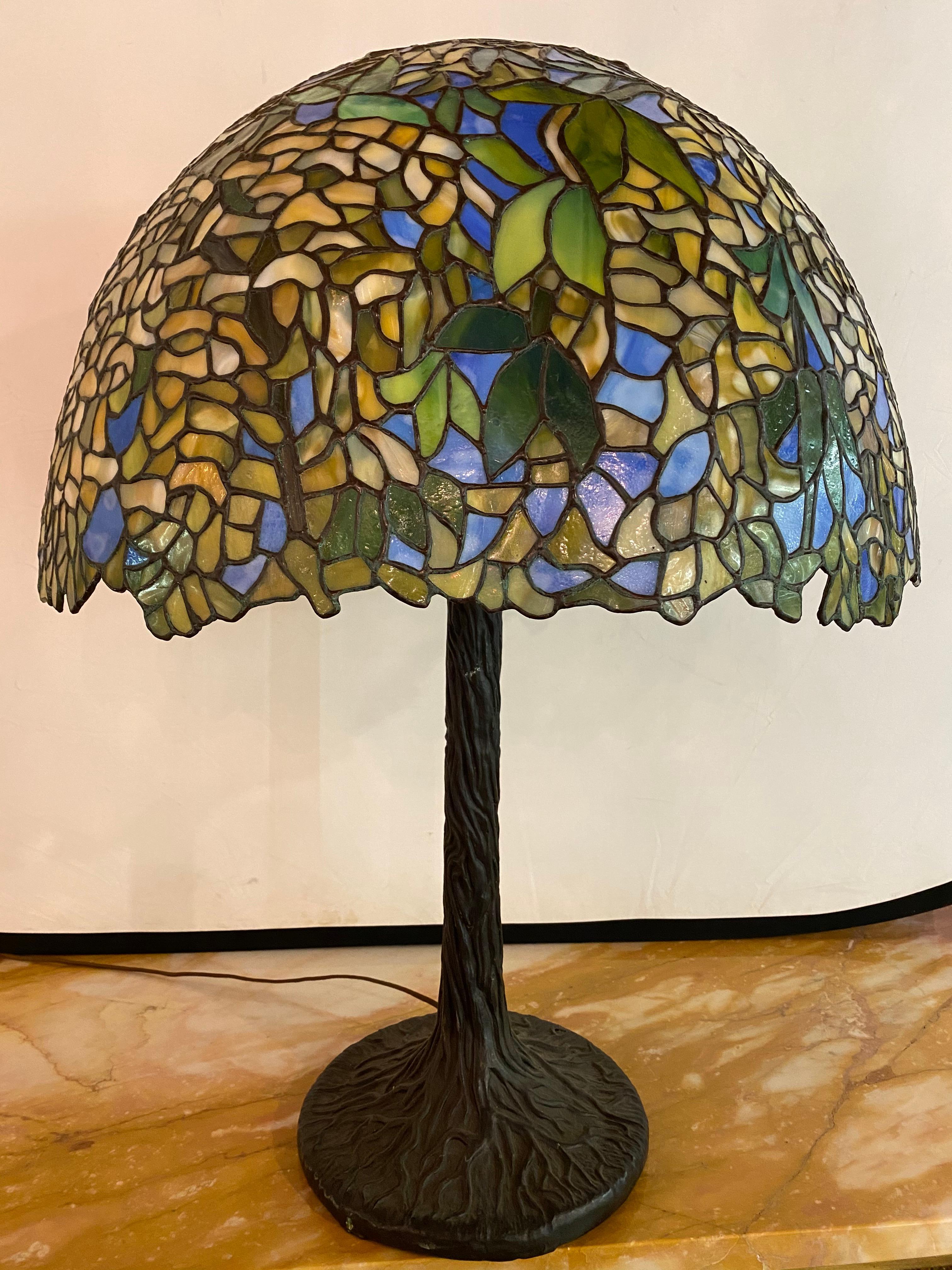 Large green floral Tiffany style table lamp on bronze base. This vintage stunning example of Tiffany stained glass is a finely designed having a wonderful domed shade on a bronze table base. The base holding two bulbs.


SXXX-EX.