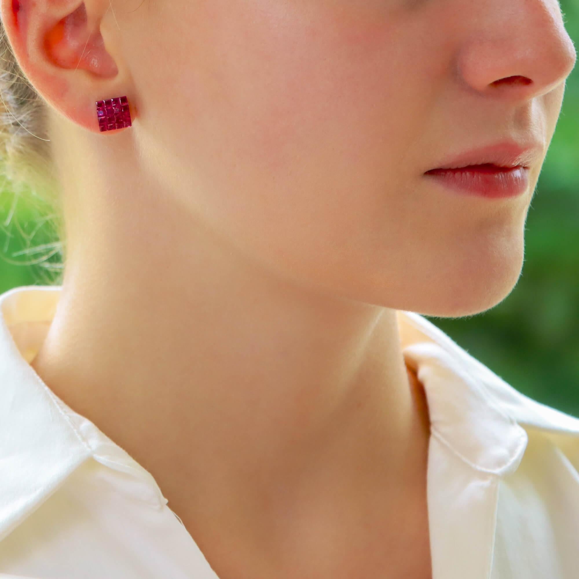 An elegant pair of invisibly set ruby square earrings set in 18k white gold. 

Each earring features four rows of princess cut rubies seamlessly invisibly-set in an open-back white gold collet with pierced open galleries. The colour of the rubies
