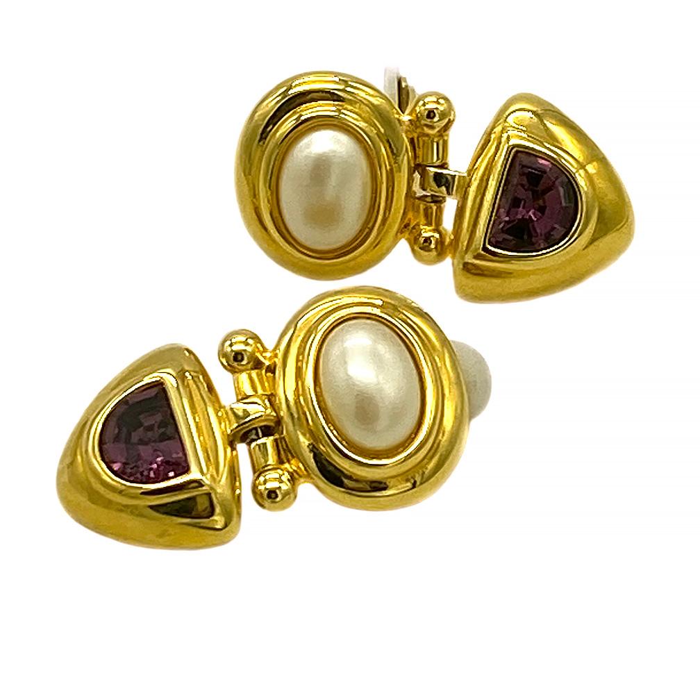 Dies ist ein Paar 1990er Art Deco Stil Joan Rivers Clip-on Ohrringe. Eine große ovale simulierte Perle und ein facettiertes violettes Kristallglas sitzen jeweils in zwei Teilen aus goldfarbenem Metall, die mit Scharnieren verbunden sind. 

Als