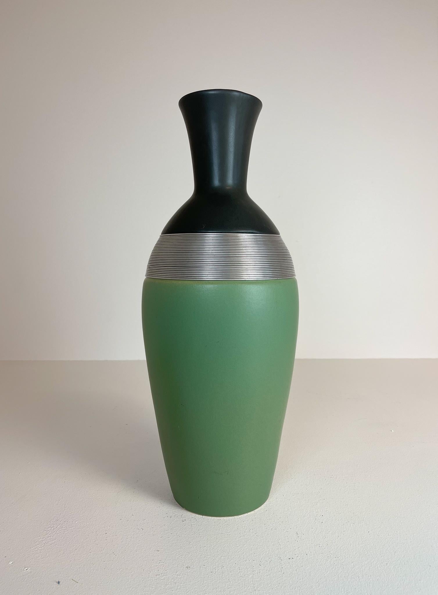 Ce grand vase de sol de style Art déco est de couleur vert mat avec des fils métalliques menant à un sommet noir. 

Bon état vintage. 

Dimensions : H 52 cm D 22cm.
  