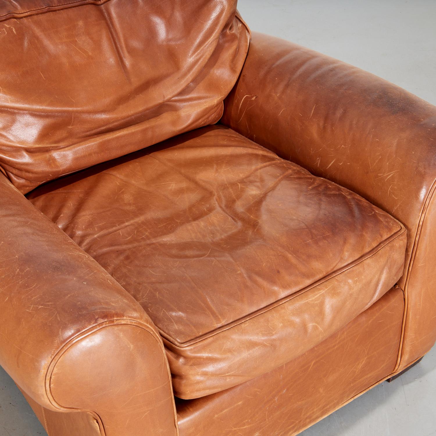Mid 20th c., Art Deco style tobacco saddle leather club chair with short wood feet, an attached back cushion and loose seat cushion, unlabeled.
A very comfortable chair. It has a slouchy appearance, suggesting many hours were enjoyed seated in this