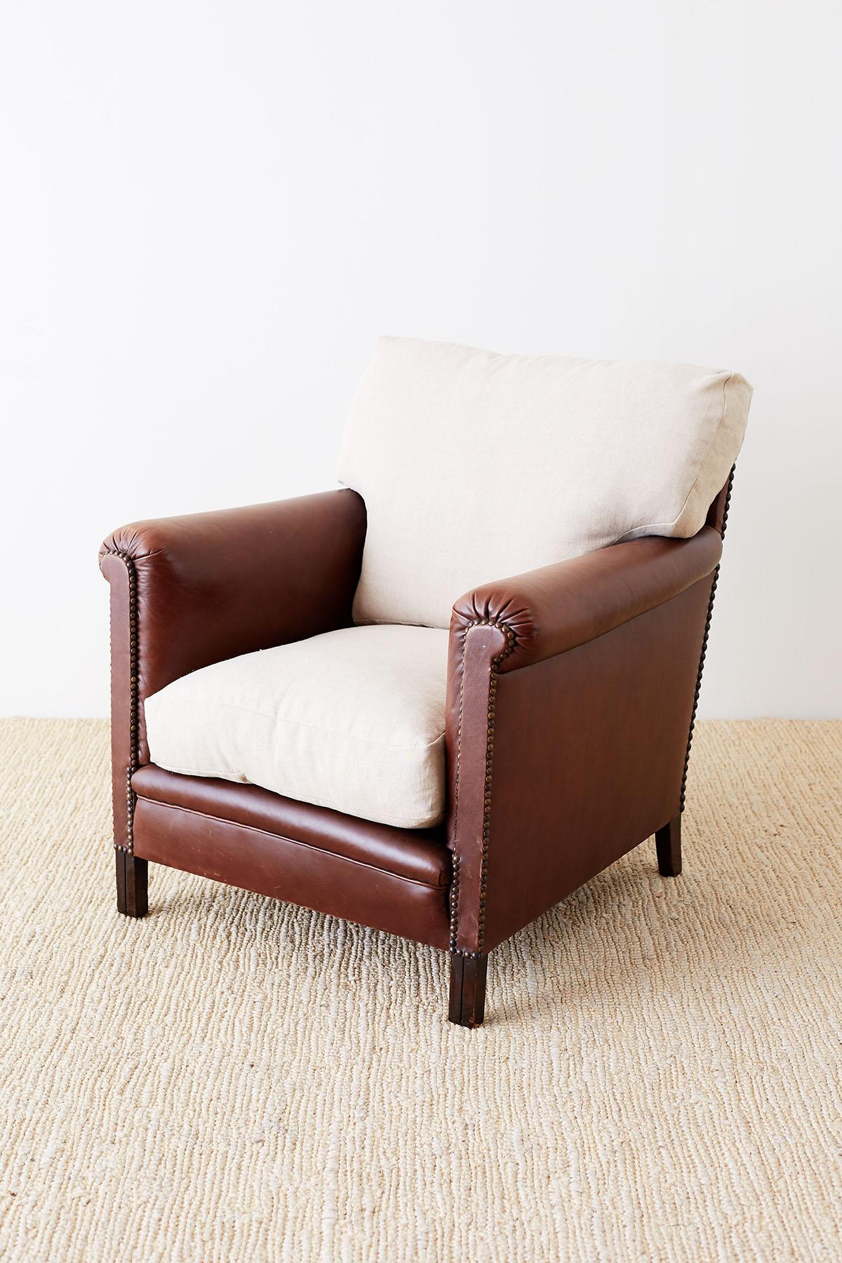 American 20th century leather club chair or lounge chair made in the Art Deco taste. The chair features a deep seat with flat, straight arms that are subtly rolled on the top. The generous seat has thick, fitted loose seat cushions that are down