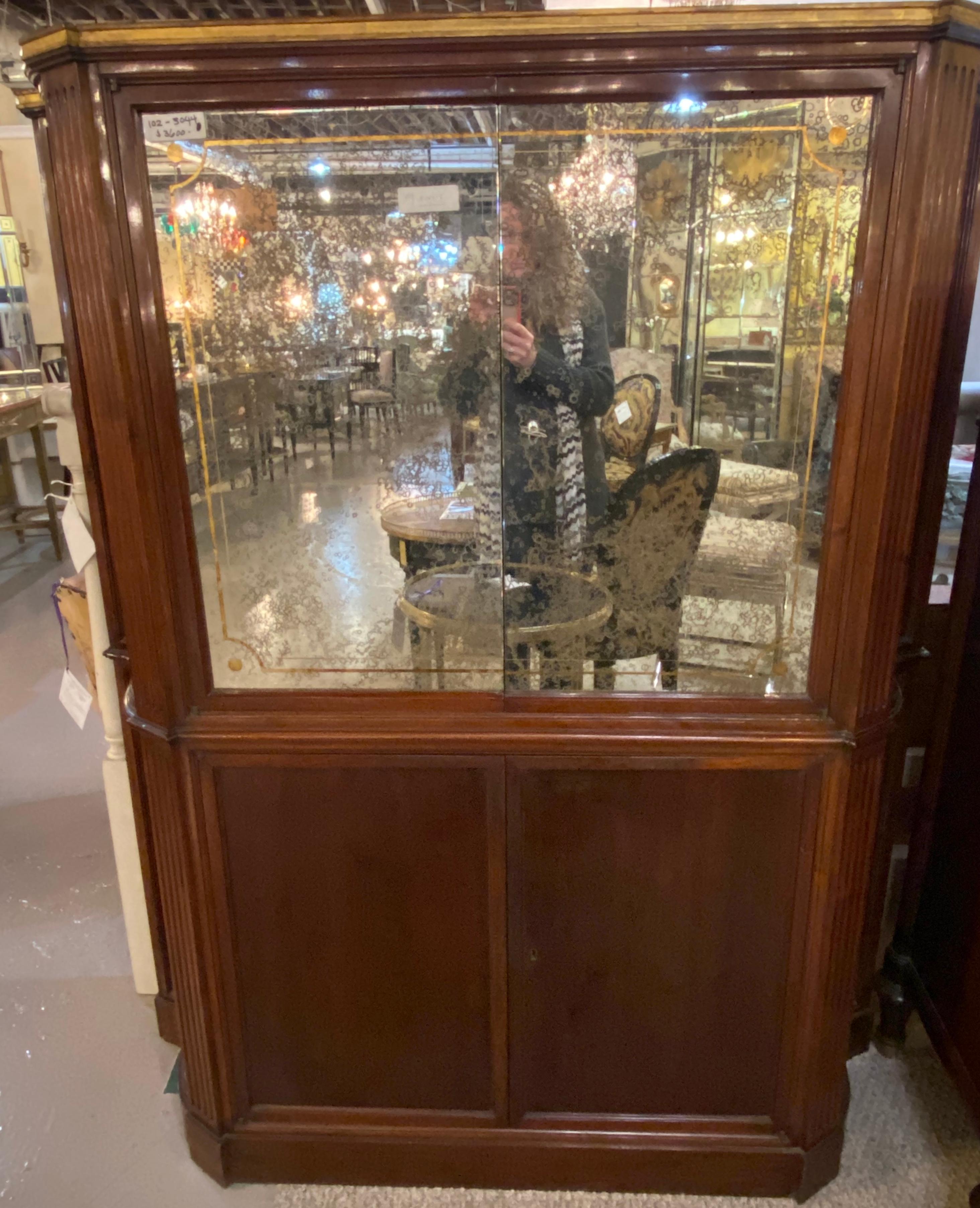 An intriguing mahogany French bar or serving cabinet, circa 1940s in the Art Deco style, the top with distressed mirror veneered doors, opening to a glass shelving and mirrored interior, over a conforming case fitted with sets of small and narrow
