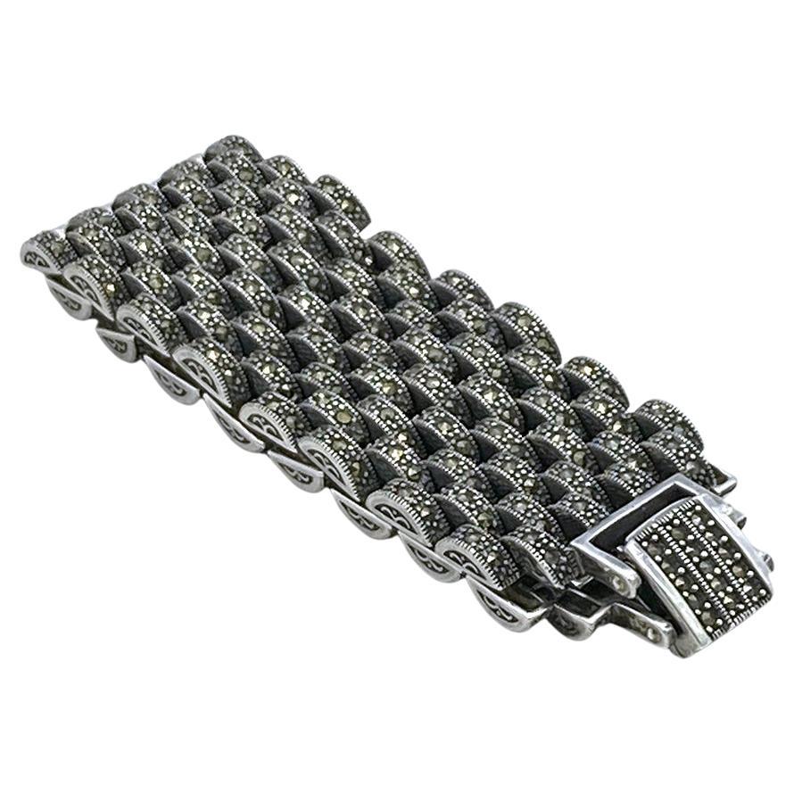 This is an Art Deco style marcasite sterling link bracelet. This over 77 gram bracelet has nine rows of small marcasite encrusted segments linked together with a fold over clasp. It could be worn by a small wristed man. It was crafted by a Thai
