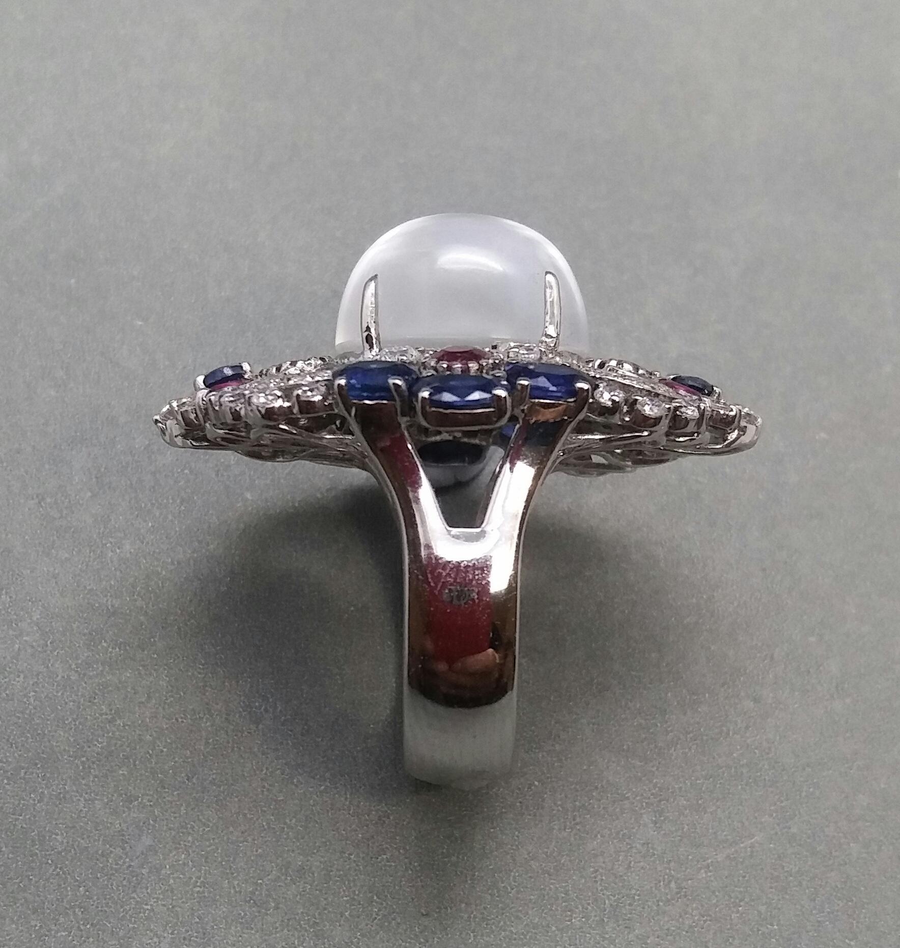 Unique and completely handmade 14 kt white gold ring,with a central Moonstone cabochon measuring 12x14 mm,surrounded by 4 mm round faceted rubies of 4 mm diameter,8 mm oval blue sapphires of 3x4 mm,4 small faceted round rubies of 2,5 mm. and 1.5