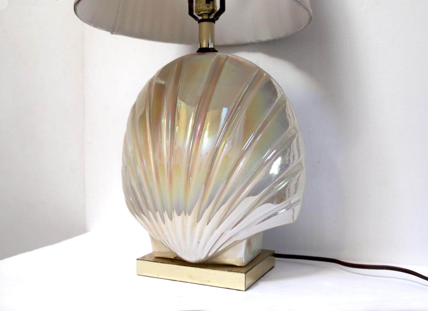 Form nearly matches function in this art deco style lamp with its pleated shade. The symmetry is apparent from the graceful base in its half-shell silhouette which seems to point toward the lampshade. The lamp base is an eggshell white color that is