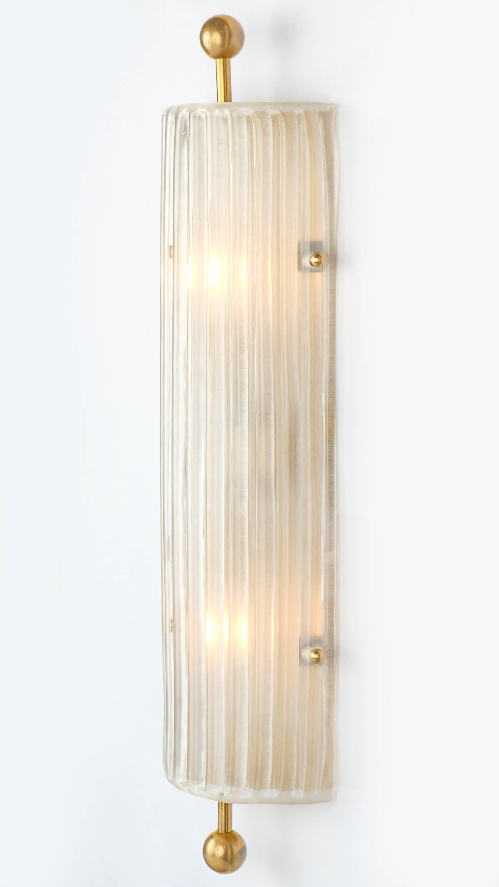 Una coppia di eleganti appliques in vetro di Murano e ottone in stile Art Déco. Questi pezzi d'illuminazione da incasso hanno una struttura senza tempo che viene esaltata dal vetro di Murano a coste, testurizzato e smerigliato. Ogni applique