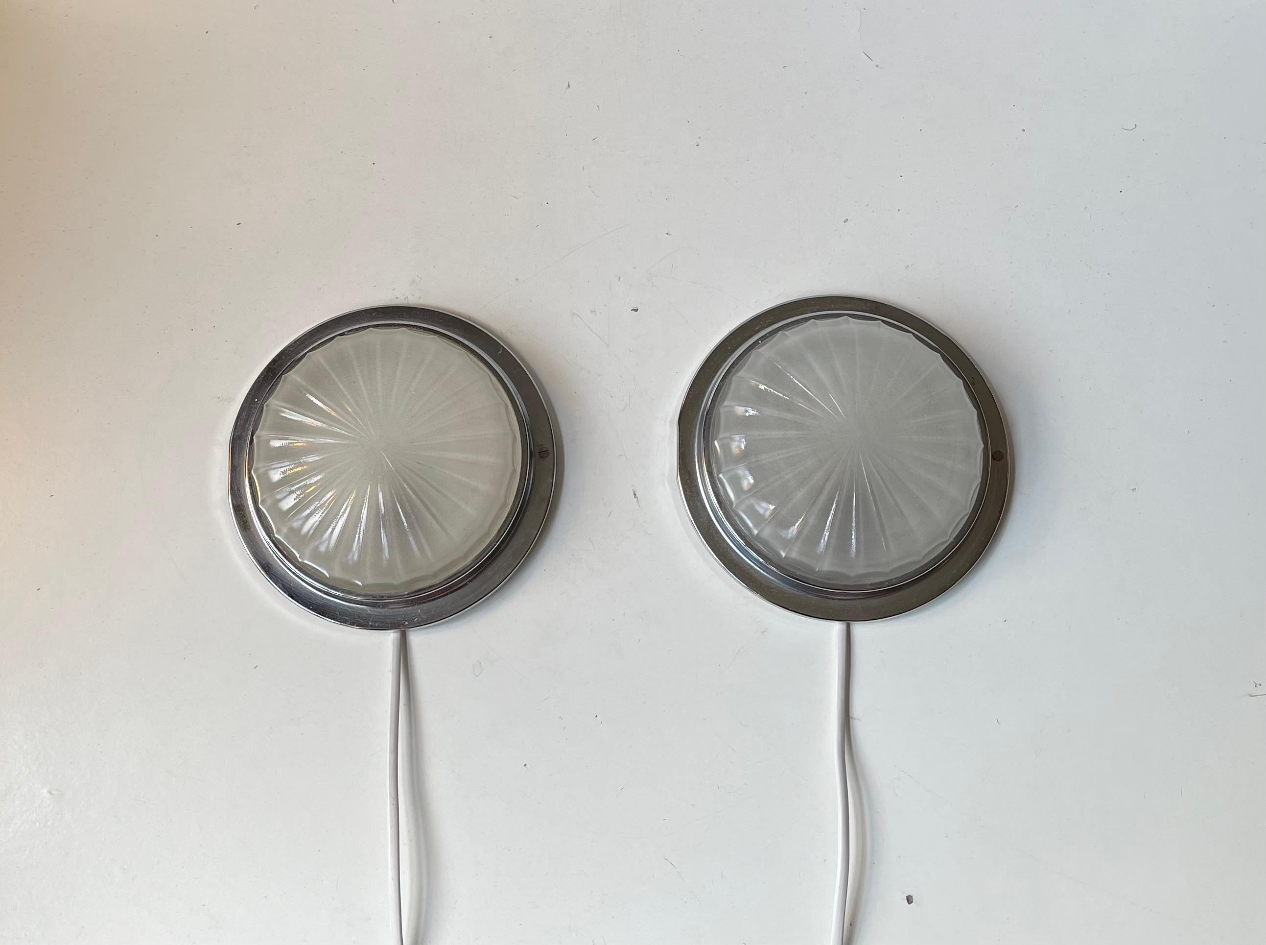 A pair of fixed wall lights in a nautical art deco style. Designed and made by BMAC in Hyde England circa 1960 for an English State Ship where these also came from. The are made of nickel/chrome-plated metal and has a shell like sunburst motif to