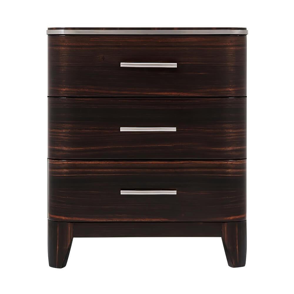 An Art Deco-style nightstand inspired by 1930s luxury. This three-drawer chest with a rounded edge top with polished nickel trim, exotic Amara veneers with polished nickel finish handles, on tapering legs, with soft closing drawers.

Dimensions: 22