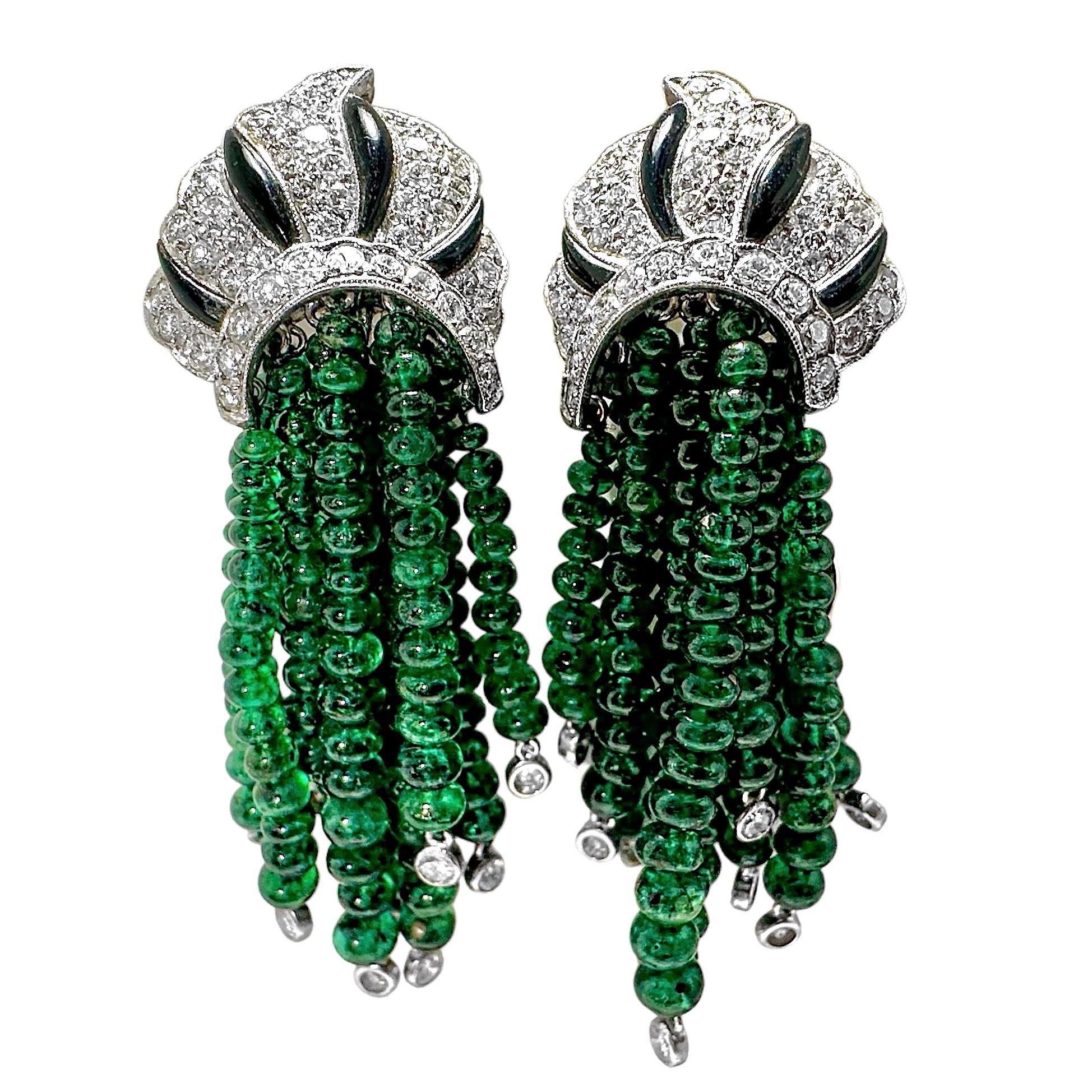 A pair of antique style earrings in white gold featuring hanging, strands of emerald beads. Each strand terminates in a bezel set round brilliant cut diamond. The tops of the earrings have a royal appearance, with assorted round brilliant cut