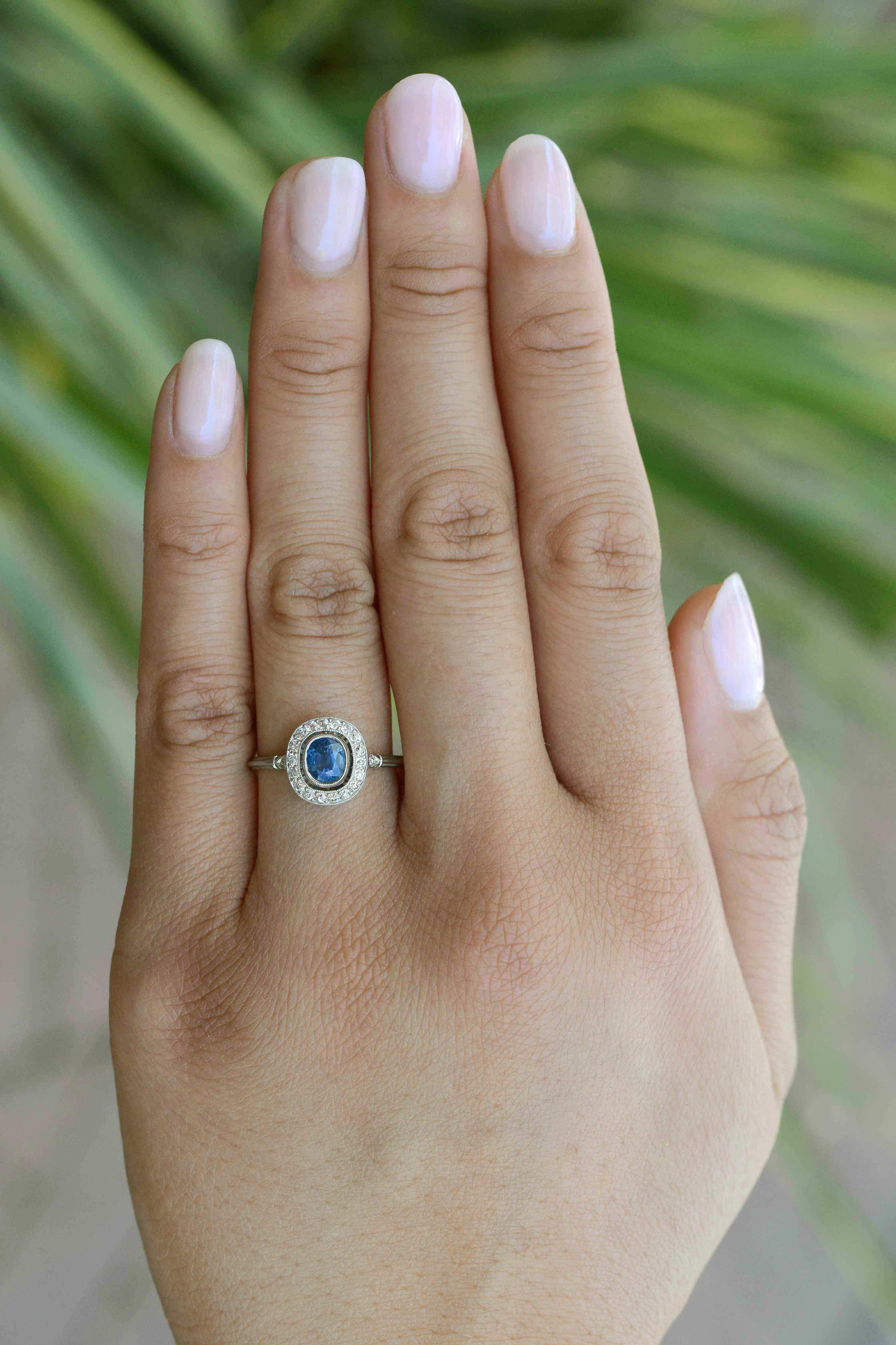 Sitting regally in a millegrain bezel, the velvety, navy blue sapphire commands attention with a twinkling surround of diamonds in a low setting of pure platinum in this quintessential Art Deco revival gemstone engagement ring. Sapphire symbolizes