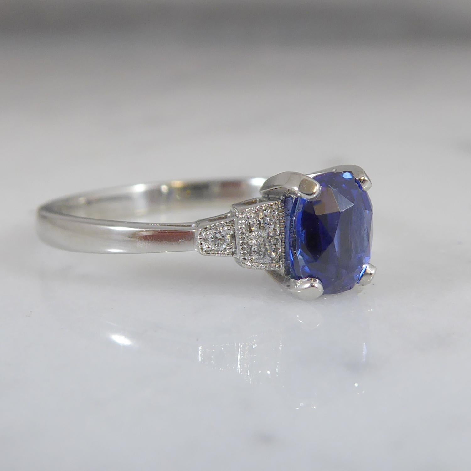 Oval sapphire  and diamond ring has echoes of the Art Deco era.  Set with an oval, mixed cut sappire 1.16ct,  of rich blue colour held in four white claws to stepped shoulders each featuring three diamonds in individual millegrain edged box