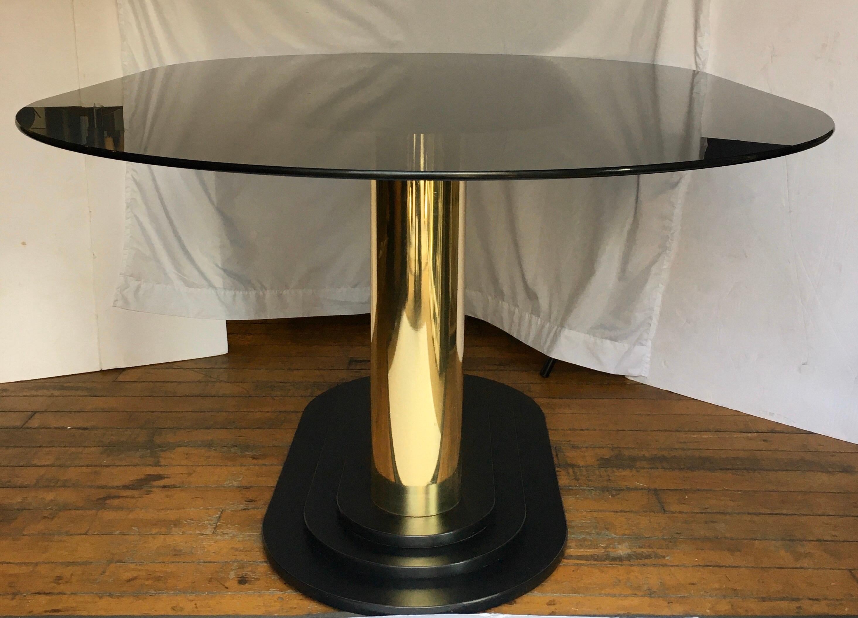 Art Deco style oval dining table featuring a removable smoked glass oval top and a reflective gold double column pedestal base. This modern sculptural piece would also make a stylish center table. Coordinating brass dining chairs also available for