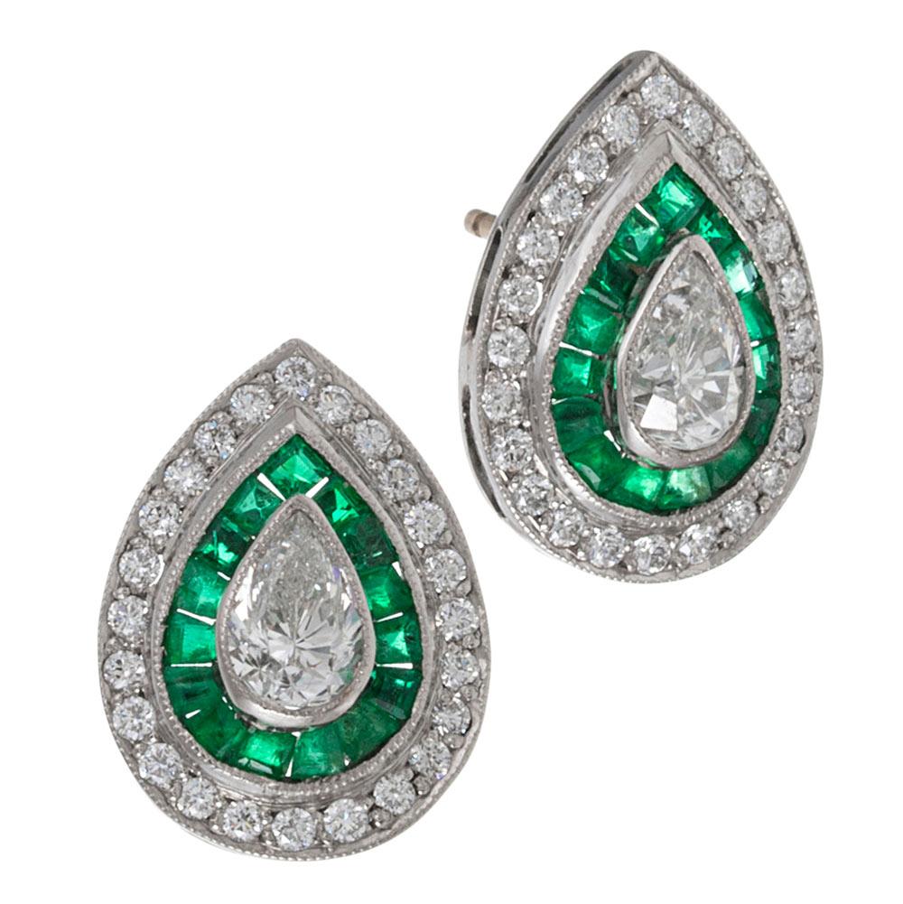 These teardrop-shaped ear studs centered upon a pair of pear brilliant white diamonds, framed in a rippling halo of emeralds and brilliant diamonds are handmade in classic art deco tradition, yet are of more modern manufacture, offering spectacular