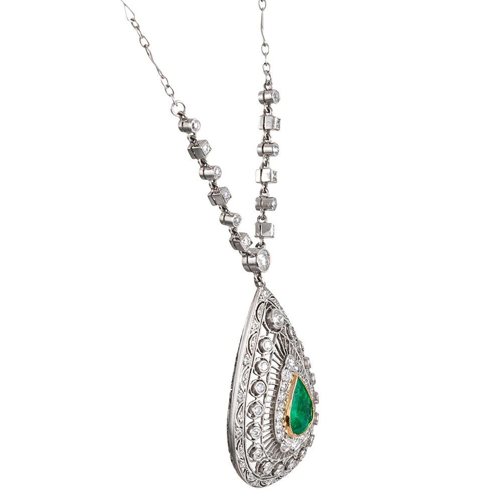 Offering the artful handmade quality of traditional art deco design with the superior physical integrity of more modern manufacture, this lacy platinum pendant features a 1.40 carat pear brilliant emerald set at its center in 18 karat yellow gold.