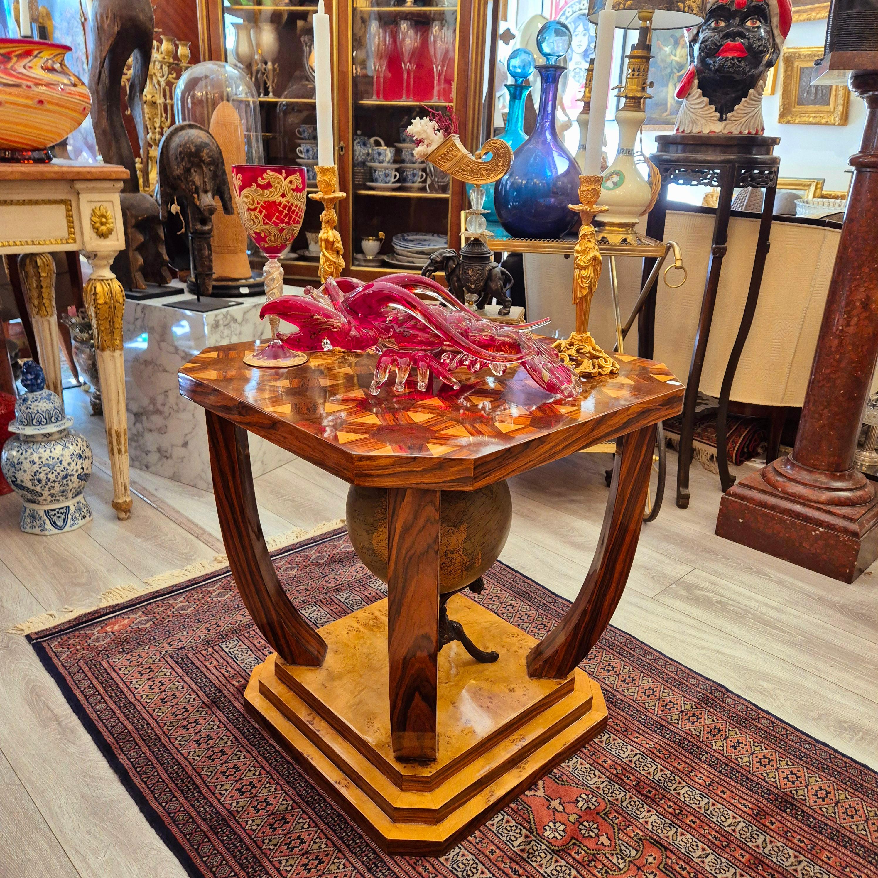 Mesa auxiliar de estilo Art Déco realizada en los años 80 en madera de palisandro y rebabas de olmo barnizadas. La parte superior de borde biselado descansa sobre cuatro patas estrechas y arqueadas, unidas por una base escalonada que reproduce la