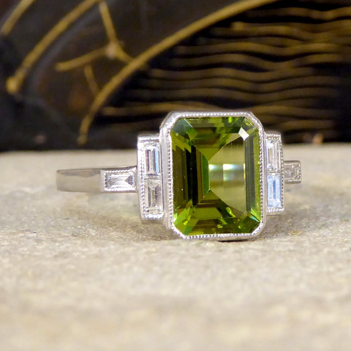 Introducing our Art Deco-inspired Peridot Ring—a harmonious blend of vintage elegance and contemporary flair. Set in the enduring beauty of platinum, this ring features a vibrant Emerald cut peridot as its centre piece weighing 2.30ct, capturing the