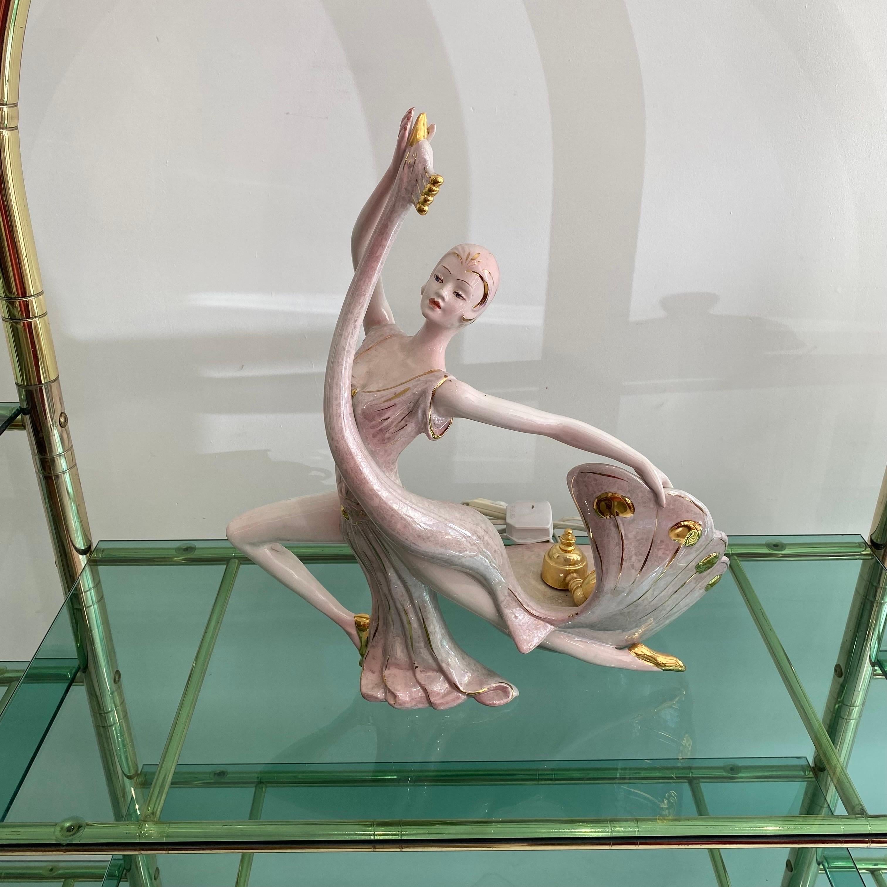 An elegant ceramic table lamp depicting a dancer with a swan dress like bird that transforms into a lamp. This piece is reminiscent of Erte fashion illustrations of the Art Deco period.
Pink and cream glazed shades with 24k gold finishing. Very good
