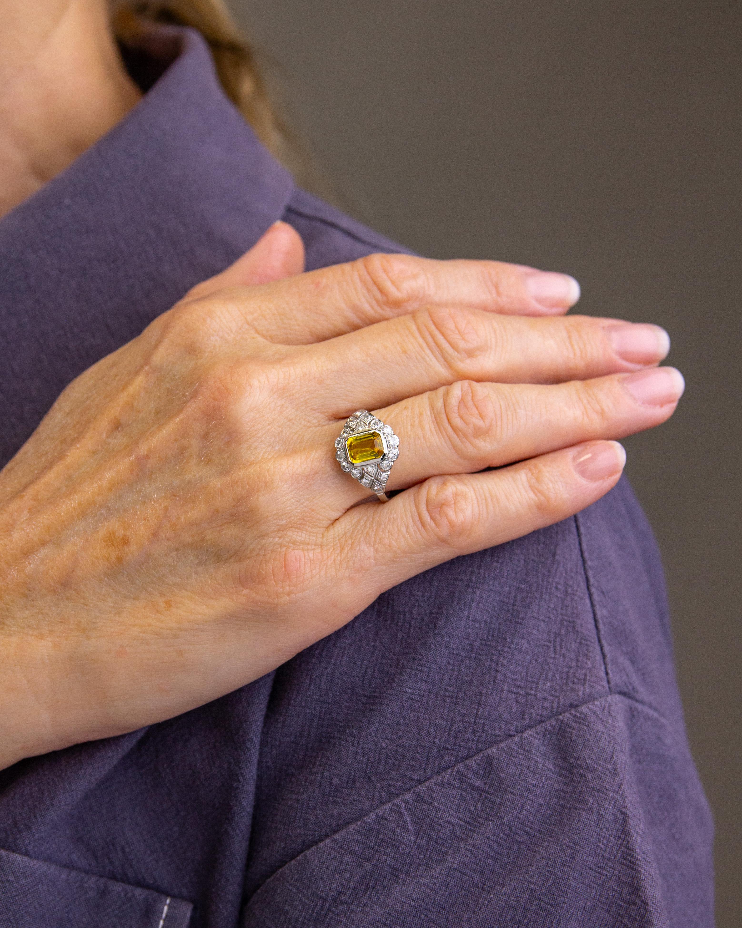 Crafted from platinum and set with a central yellow sapphire surrounded by diamonds, this ring has been made in the Art Deco taste. The platinum mount centres on an Australian type yellow sapphire which is octagonal step cut and weighs approximately