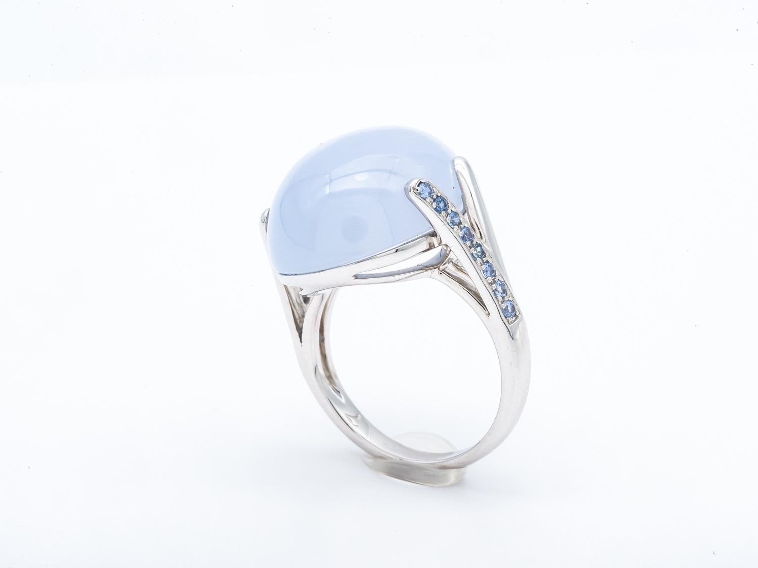 Discover the timeless elegance and charm of this Art Deco-style ring in 18-carat white gold, topped with a sumptuous chalcedony cabochon and adorned with sparkling blue sapphires. This ring is a true work of art, harmoniously blending the iconic