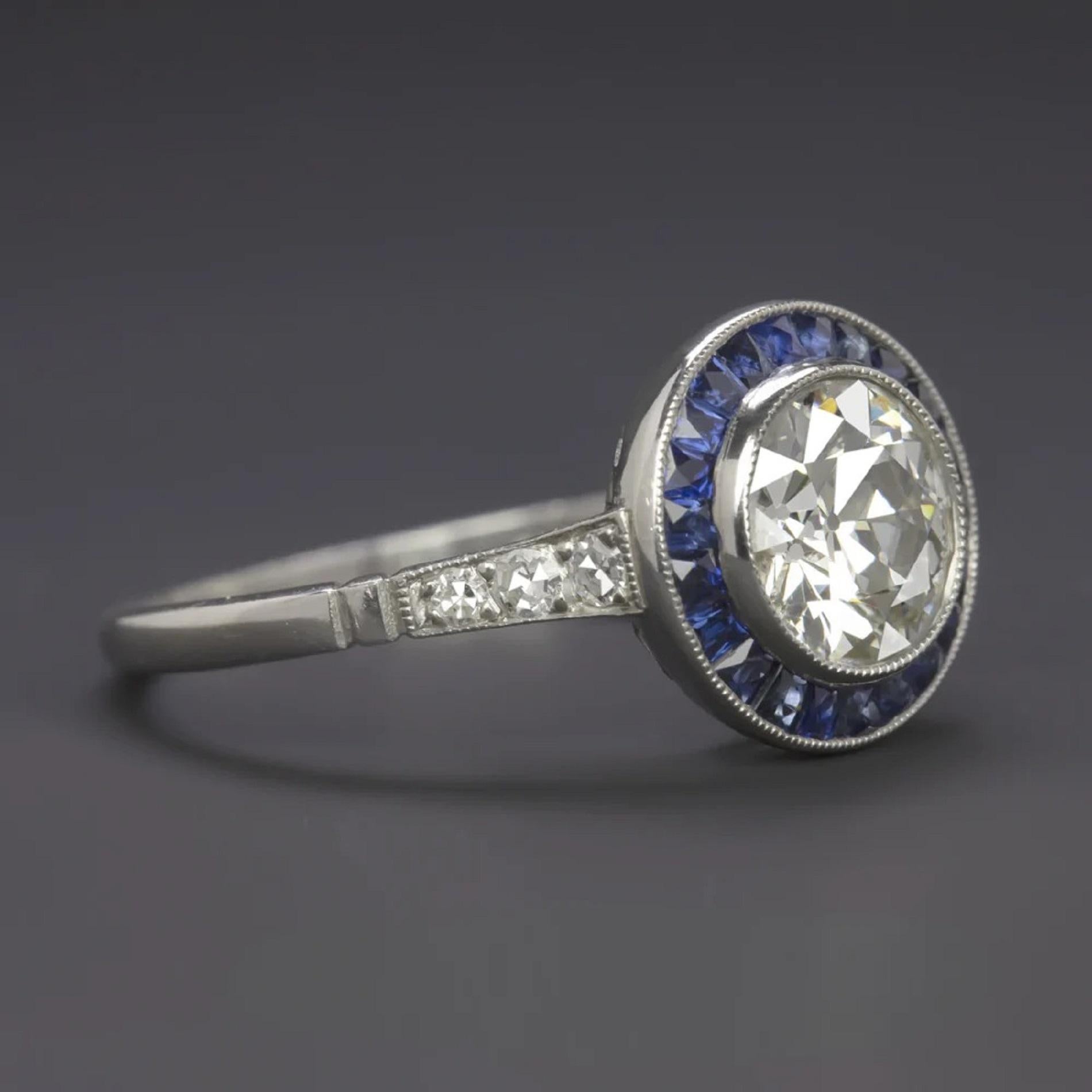 An exquisite 1.5 carat old European cut diamond surrounded by a glamorous ring of royal blue natural sapphires. Beautifully white and completely eye clean, the diamond is gorgeously vibrant. Cut by hand during the Art Deco era of the 1920s to 1930s,