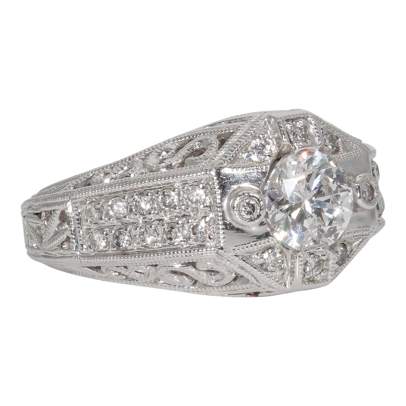 Art deco style ring in 18K WG with engraving and milgrain on the shank, pave set rounds on the sides of prong set round diamond centerstone.  D1.31ct.  (Center 1.01ct.)  Size 6.5