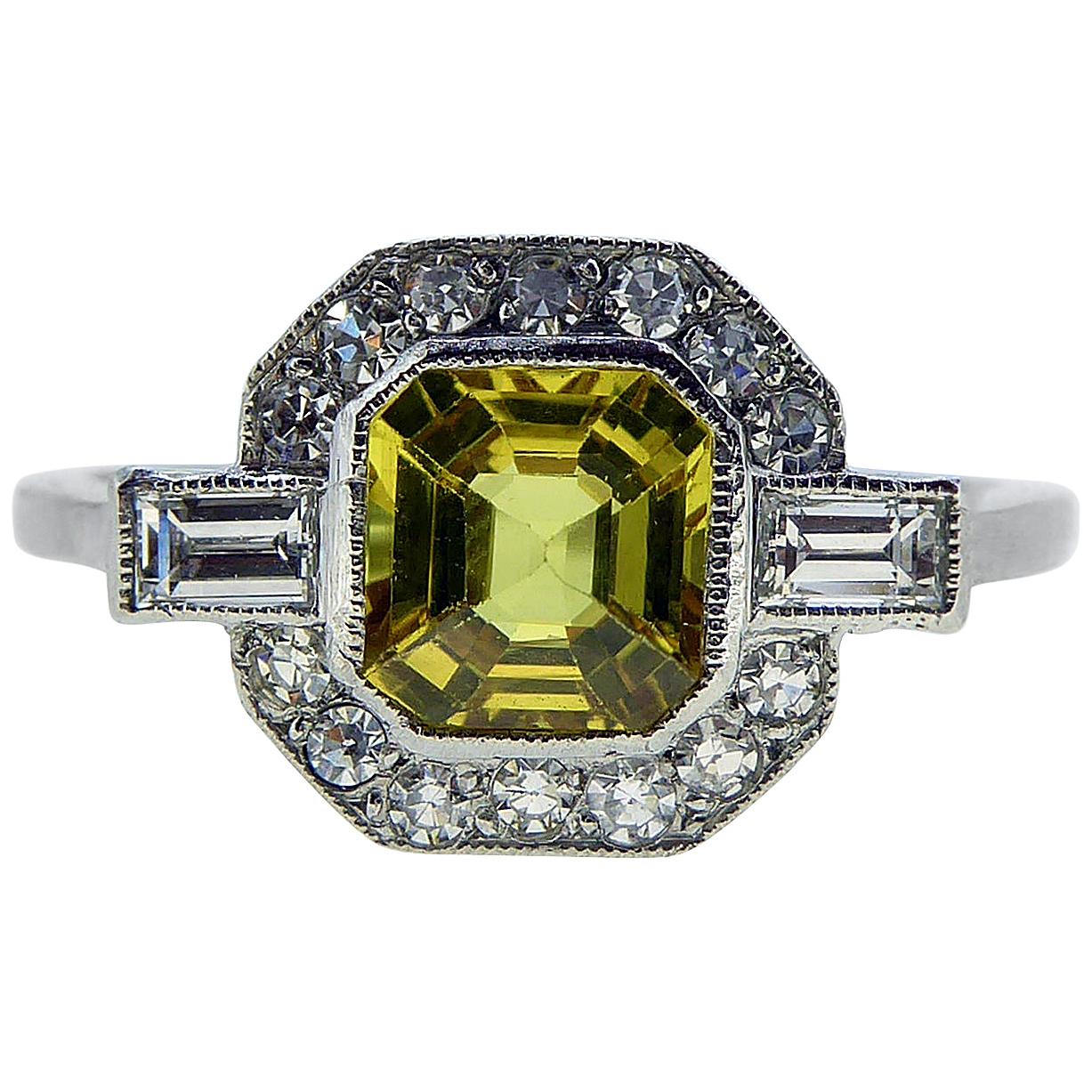 A beautiful art deco style ring in an octagonal shaped cluster.  Set to the centre with an octagonal mixed cut, vibrant yellow sapphire 1.10ct in a rub-over setting with white millegrain decoration.  A diamond border mirrors the shape of the