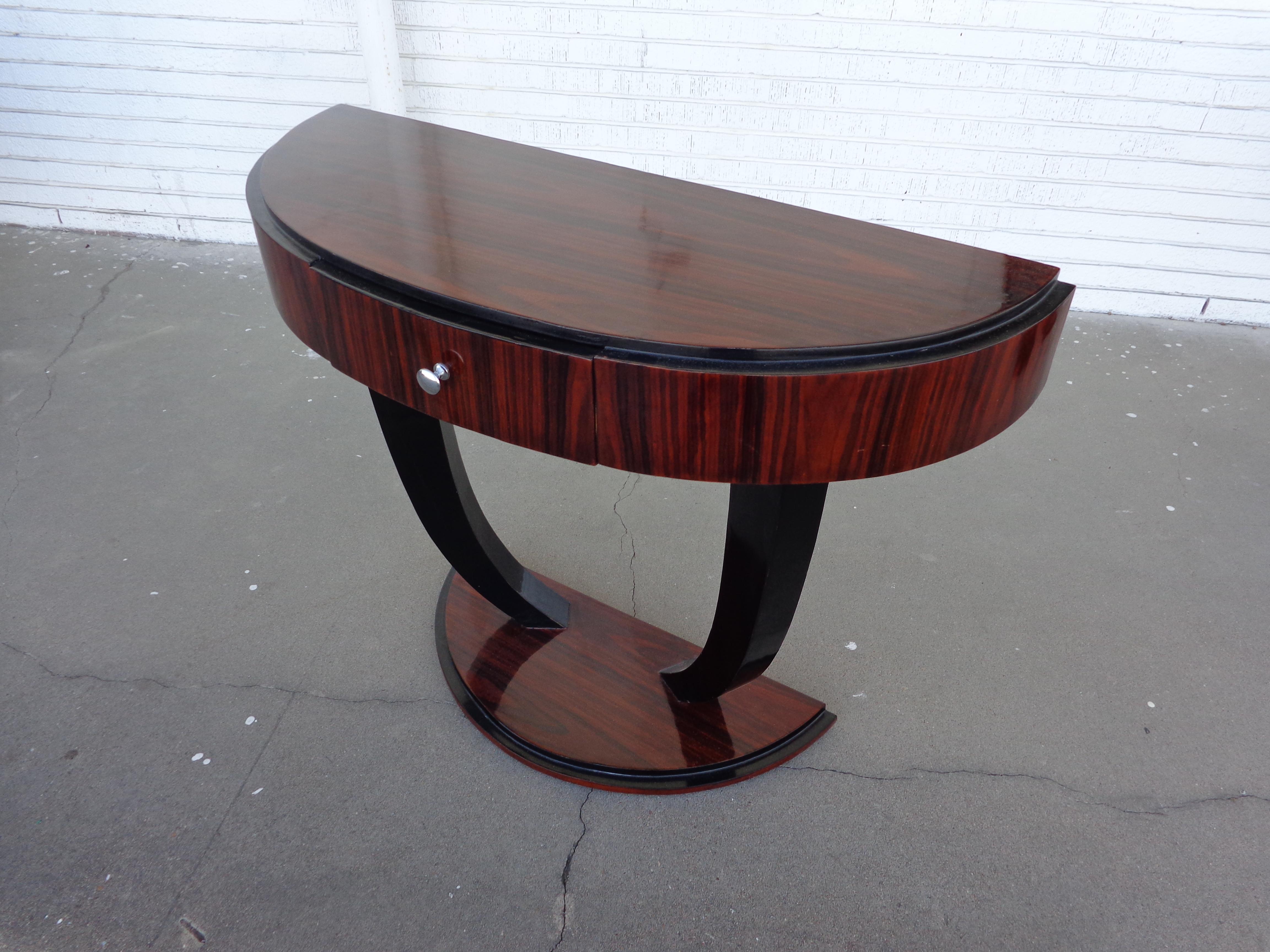 Art Deco style rosewood console table

Table features semi-oval top on ebonized arched legs on a rosewood pedestal base.
One drawer with a nickel pull. Finished back.

 