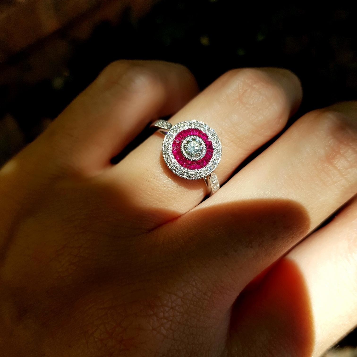 This Art-Deco engagement ring is completely spectacular! The vibrant color stone of rubies are specialty cut to surround the excellent round brilliant cut center diamond, which is in a thin bezel with mil-grain detail. Crafted in Platinum950. 

Ring