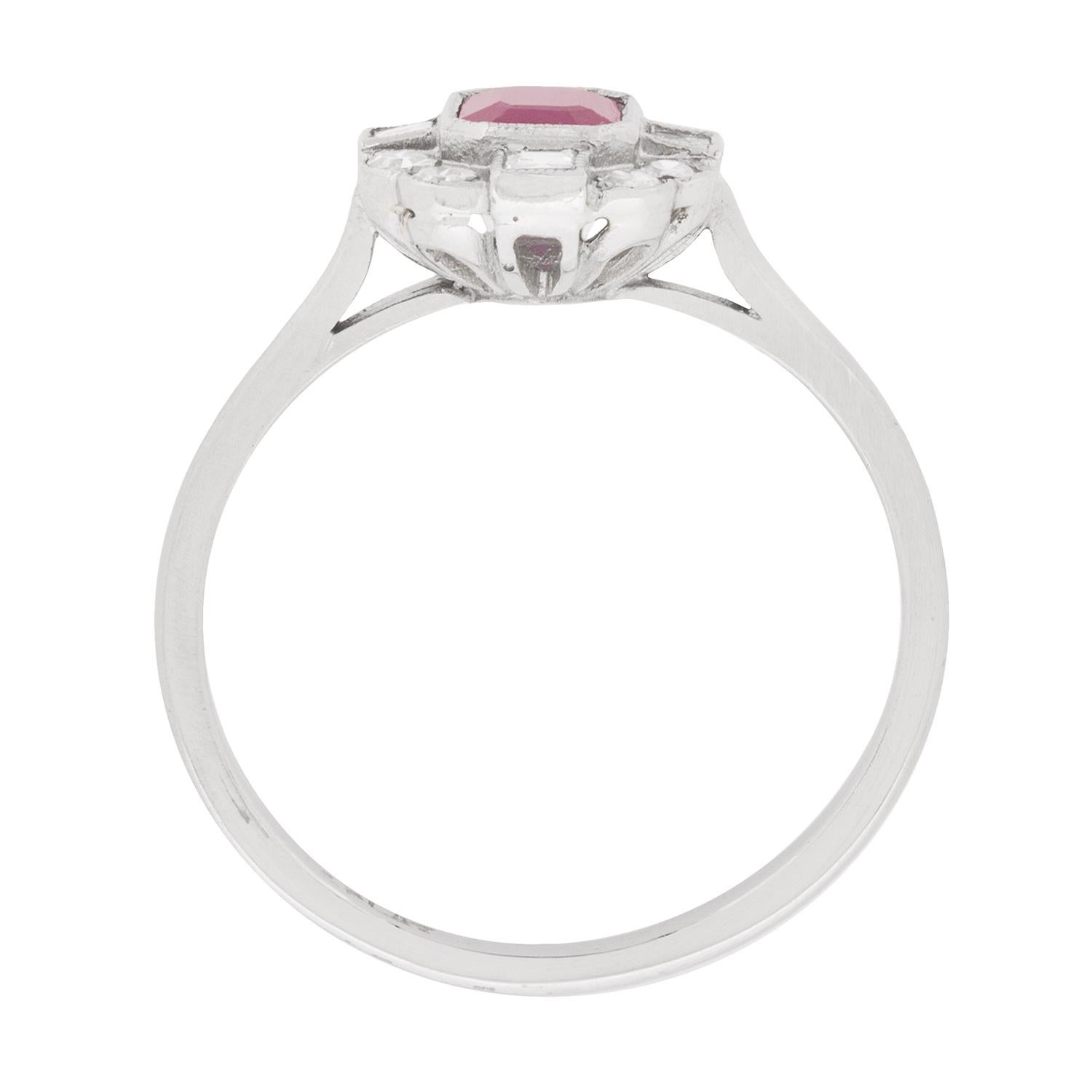 Inspired by the deco era, this cluster ring features a ruby weighing 0.65 carat and is a lovely emerald cut shape. It is a light red, which works in perfect harmony with the cluster of diamonds surrounding. The diamonds are a mix of carre cuts, set