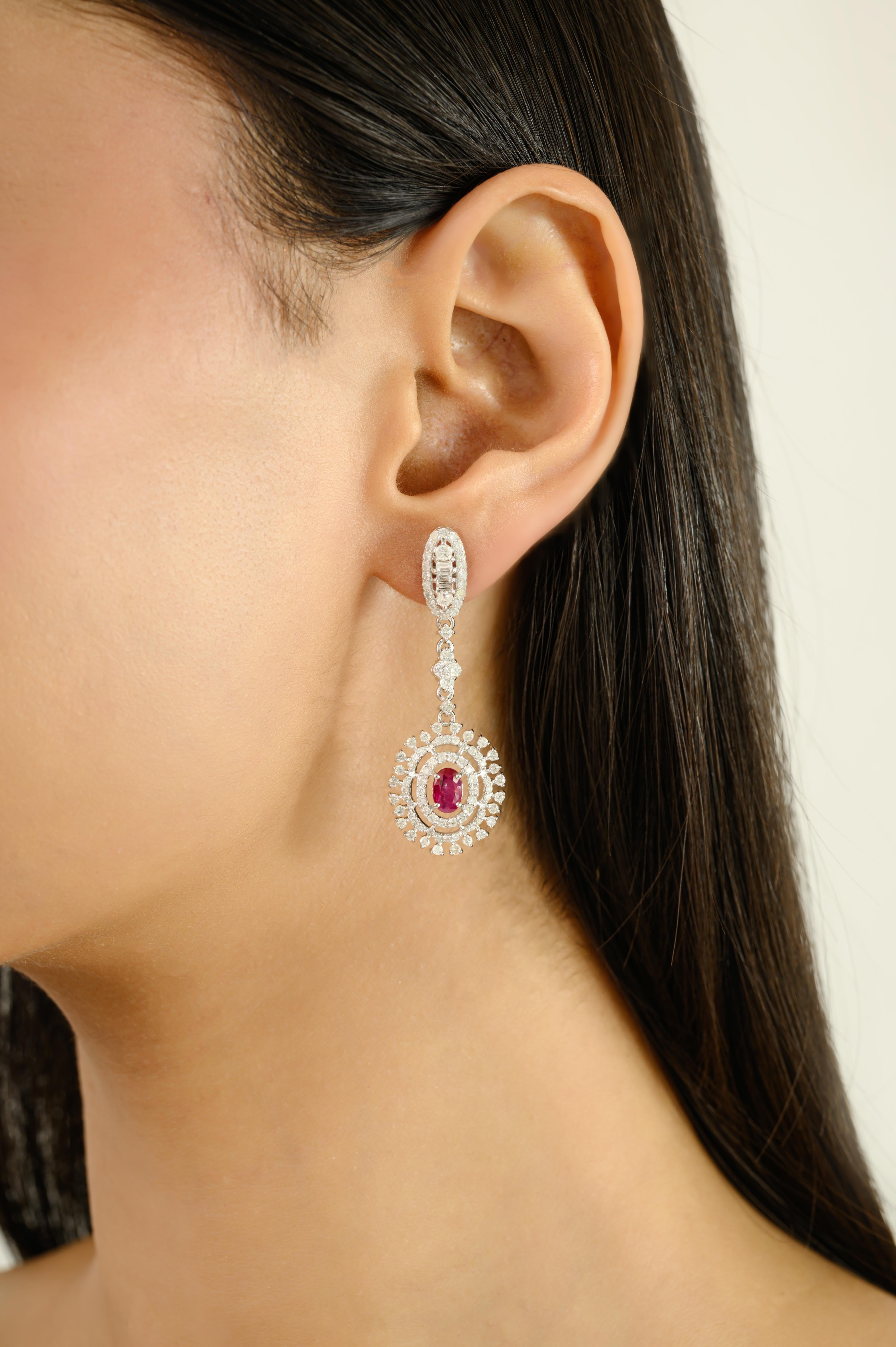 Rehaussez votre élégance avec ces boucles d'oreilles pendantes de style Art déco en or blanc 14 carats, ornées d'un halo de rubis et de diamants. Mettant en vedette de vibrants rubis de taille ovale au centre, chacun entouré d'un éblouissant halo de