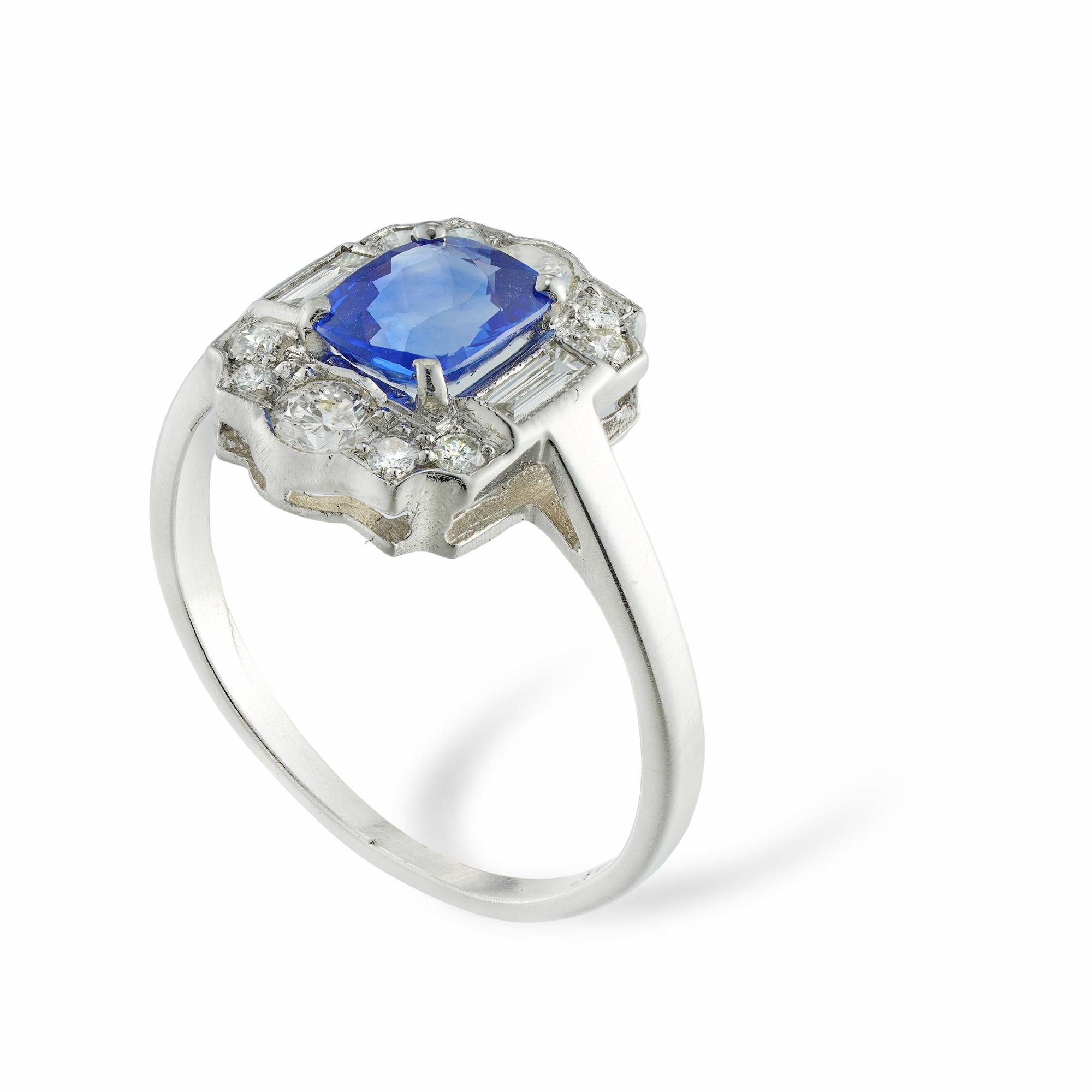 A sapphire and diamond plaque ring, the cushion-cut sapphire weighing 1.03 carats, four-claw set to a plaque with scroll and rolled-up-end shape, millegrain-set with ten round brilliant-cut and two baguette-cut diamonds, estimated to weigh 0.50
