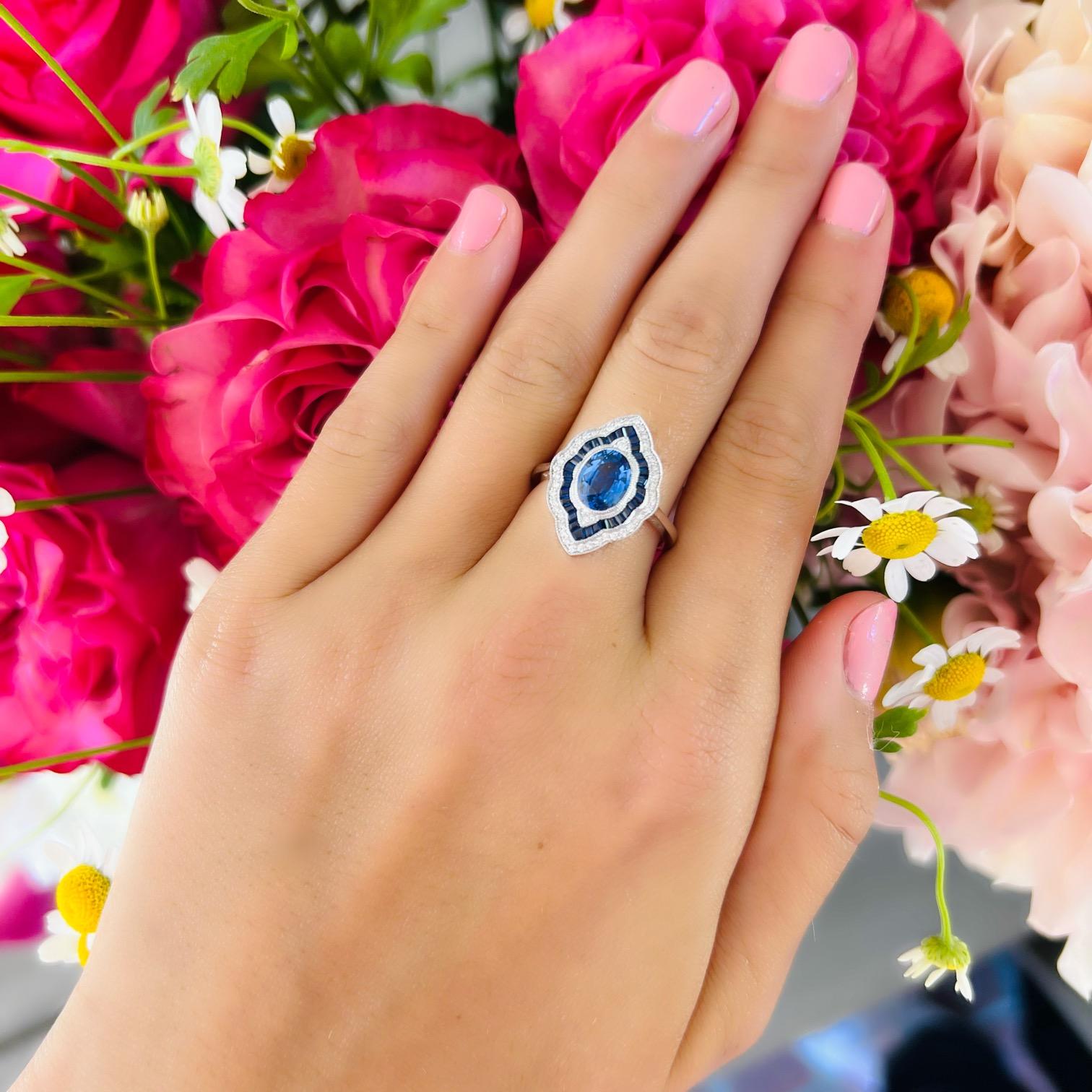 A showstopper of a ring designed to stand out in the crowd. This 14 karat white gold art deco style ring features at its center a beautiful oval cut sapphire weighing 1.44 carats set amidst .18cttw of fine natural diamonds and .55cttw of lovely