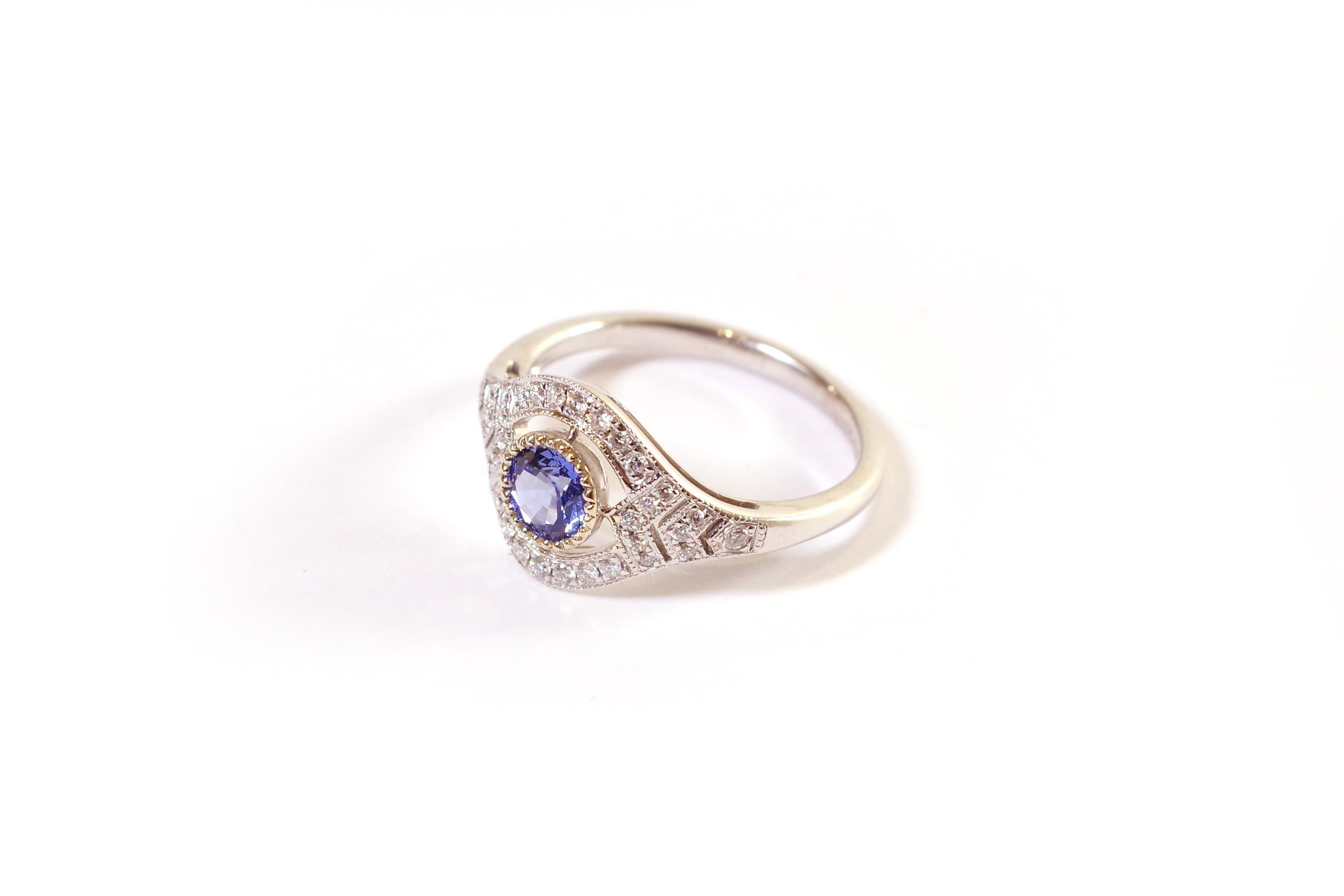 Art Deco style sapphire ring in white gold 18 karats. English ring with a circular openwork main motif, set with a round sapphire. The central sapphire is surrounded by two semi-circles of fourteen brilliant-cut diamonds. The shoulders are adorned
