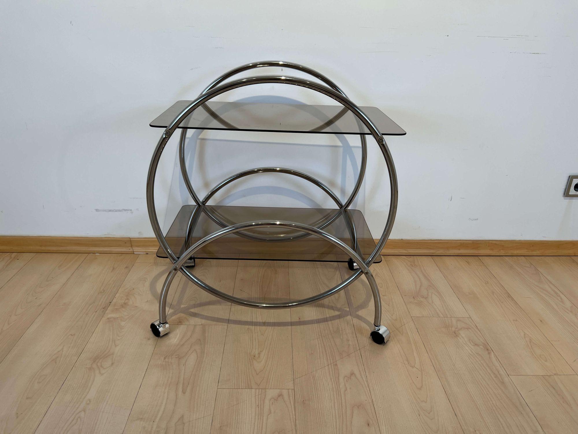 Round Art Deco Style, mid-century serving trolley from Germany around 1970.
 
Original patinated chromed steel tubes. Old smoked glasses.
 
Dimensions: H 73,5 cm x W 63 cm x D 48 cm.