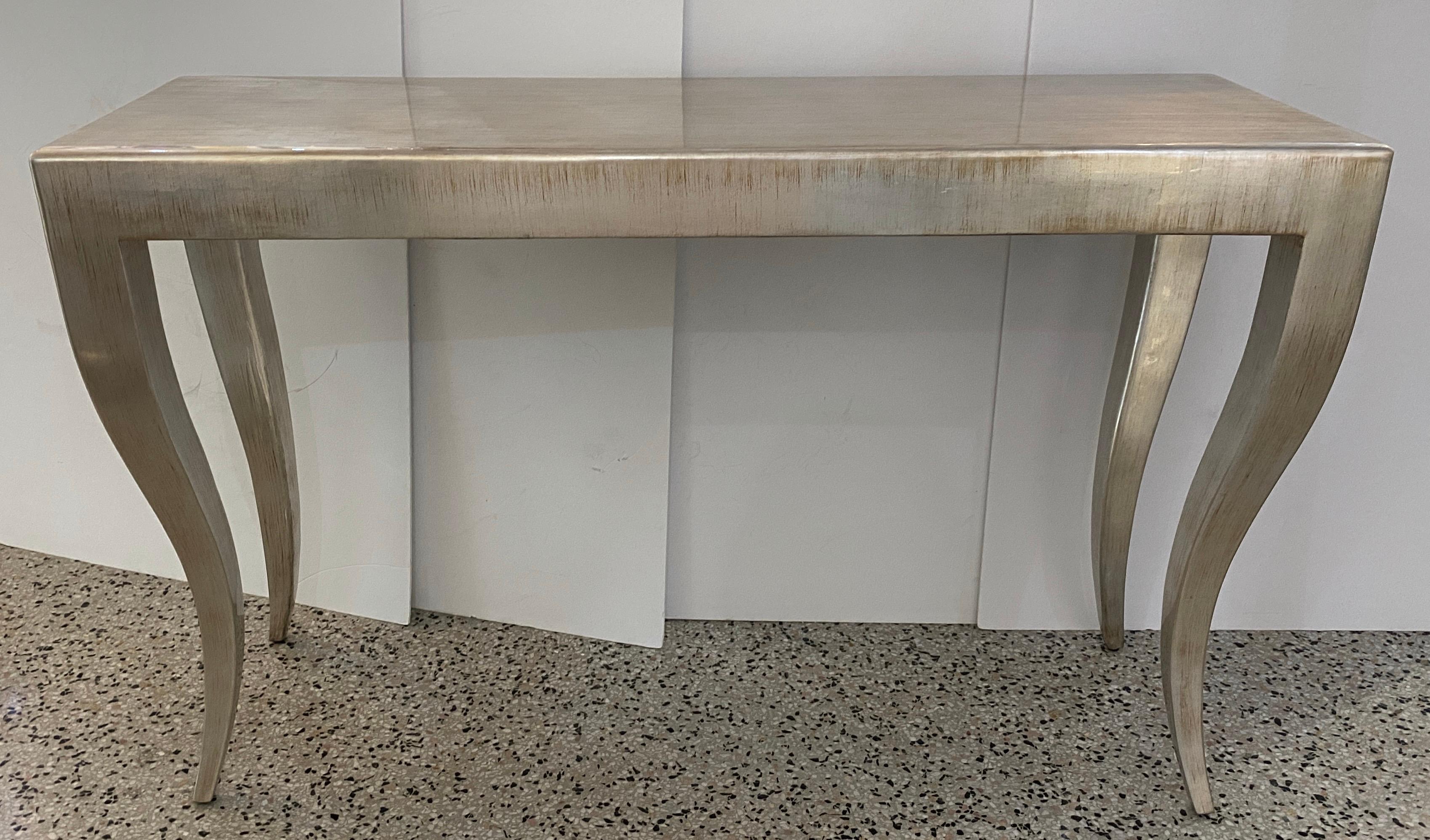 This stylish Art Deco inspired console table is finished in a silver leaf with a gold tone under-base.

Note: On two of the legs there is some bubbling to the silver leaf (see images 6 and 7), one is on the outside of the leg and the other on the