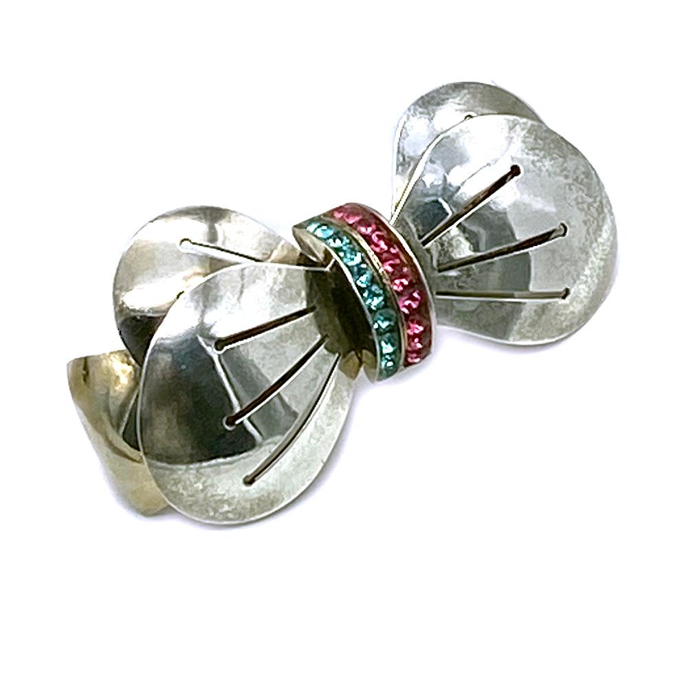 This is an Art Deco style sterling silver bowtie brooch with two rows of channel set magenta and cyan color rhinestones. An appropriate party fashion accessory for men or women. Marked Sterling on the back.

Our vintage jewelry collection and