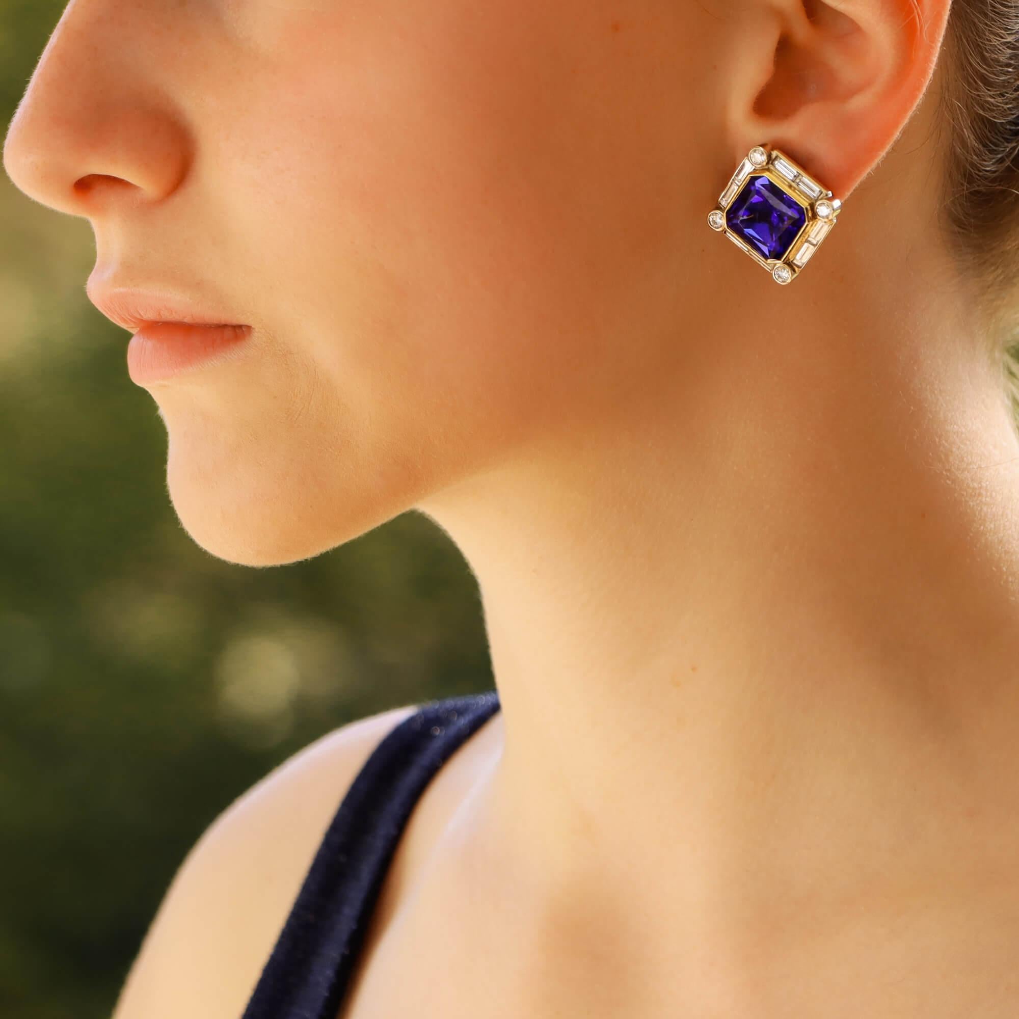 A magnificent pair of tanzanite and diamond clip on earrings in 18 karat yellow and white gold.

Each earring features a large scissor-cut (similar to square-cut) tanzanite of a deep violetish-blue colour which is rubover-set in a yellow gold