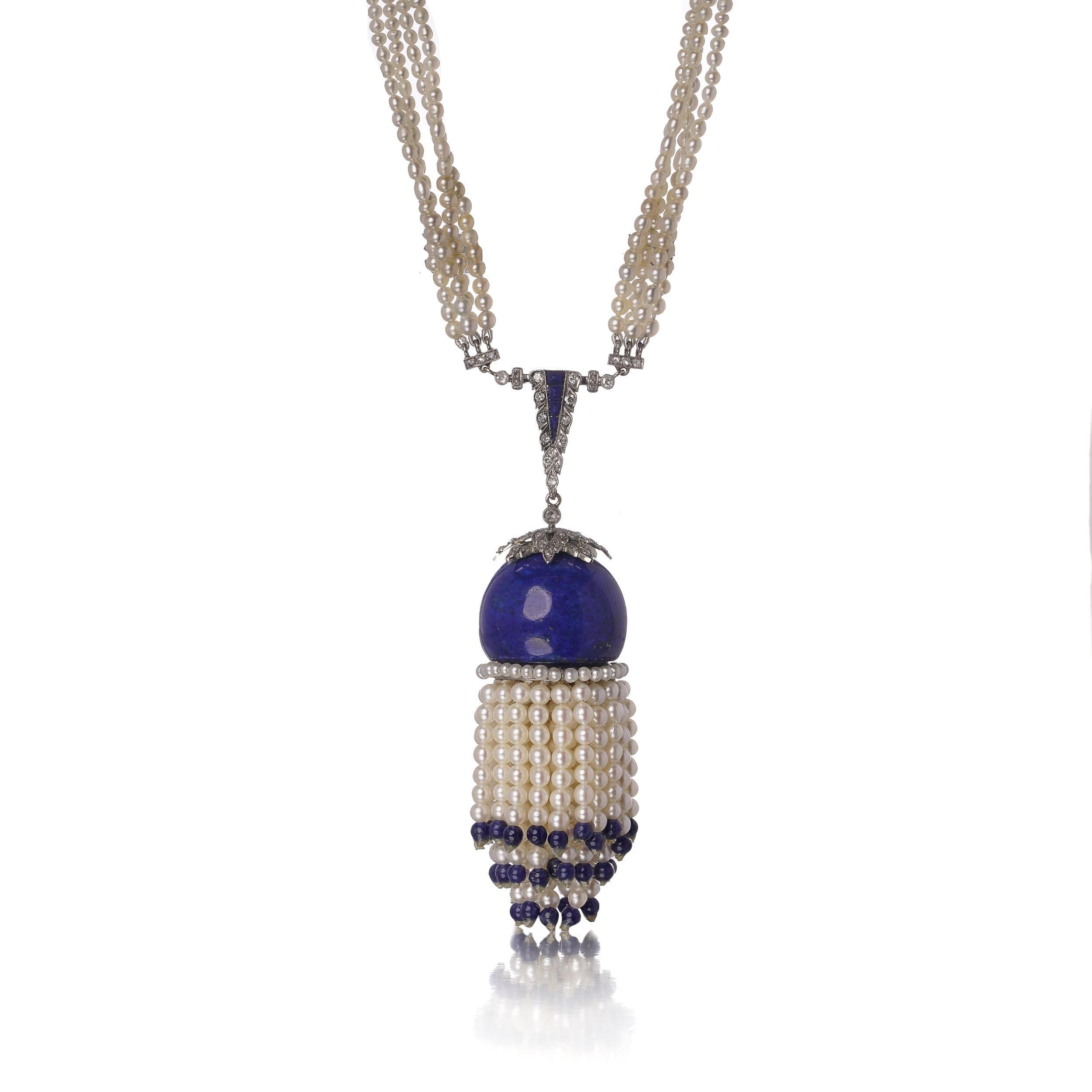 A striking Art Deco-style necklace composed of four strands of cultured freshwater pearls, terminating in a decorative tassel drop surmounted by a deep blue lapis lazuli bead. The tassel cap, pendant bail, and clasp are finely set with 42 round
