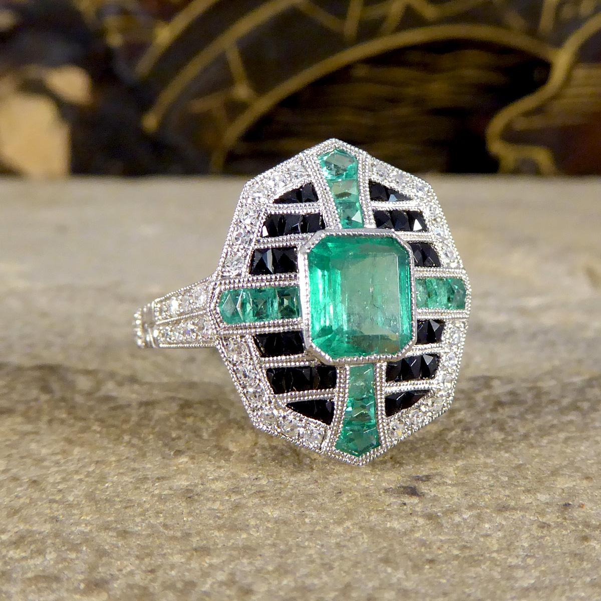 A beautifully detailed Art Deco Style ring, made in Platinum with quality craftsmanship coupled with alluring and bright stones. Set in the Centre of this ring is a 0.85ct Emerald Cut Emerald in a collar setting leading to an additional almost cross