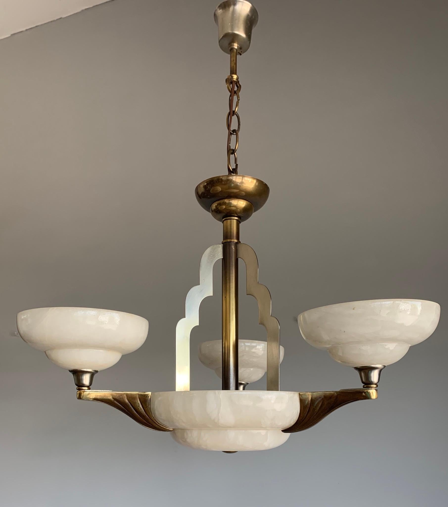 Excellent condition and great design, 3-arms and 6-light chandelier.

If you like Art Deco style light fixtures, then this 1970s alabaster and bronze chandelier could be perfect for you. The combination of the white shades and the stunning, golden