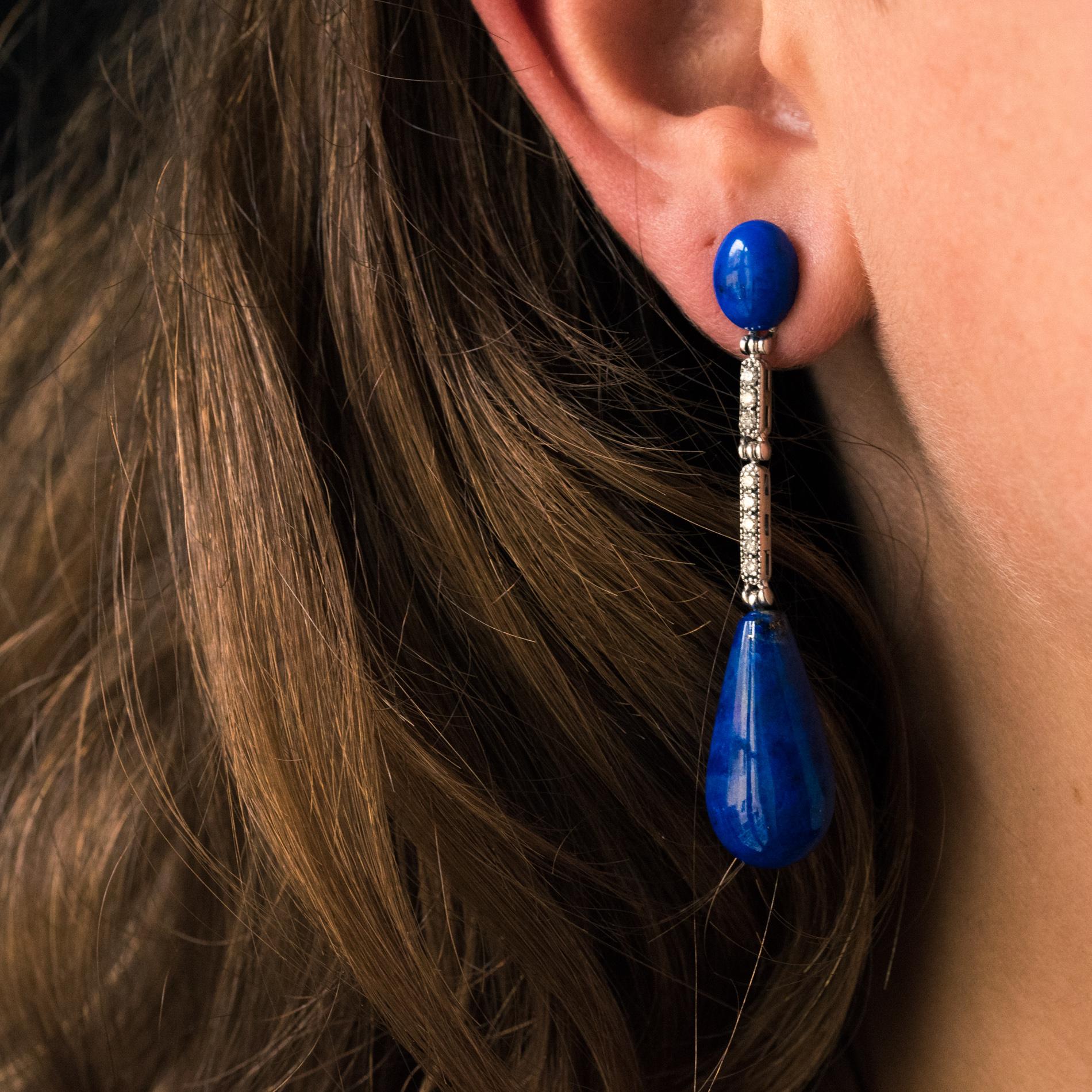 For pierced ears.
Pair of 18 karats white gold earrings.
Each of these dangle earrings consists of an oval cabochon of lapis lazuli that holds two diamond-set patterns, and at the base a long lapis lazuli pear. The attachment system is