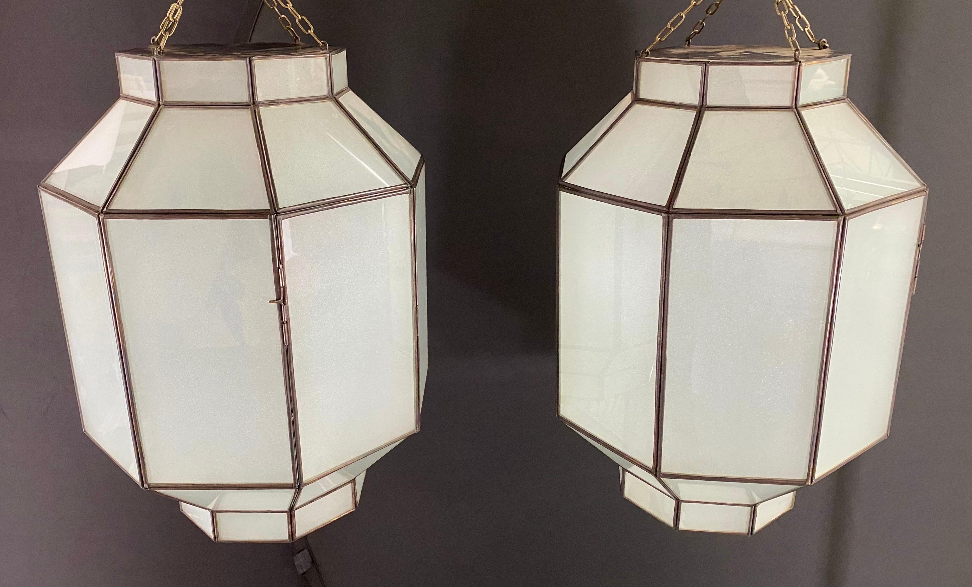 A pair of Art Deco style chandeliers, pendants or lanterns. Featuring a stylish octagonal shape, the chandeliers or pendants are finely hand-made of individual sandblasted frosted milk glass panels and patinated bronze frame. The octagonal shaped