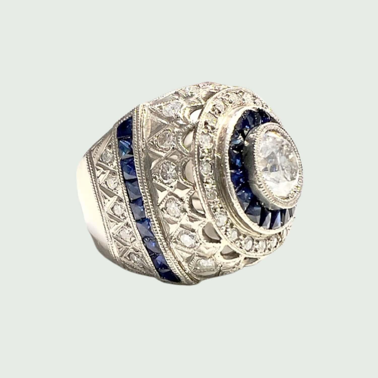 Lassen Sie sich von der zeitlosen Eleganz dieses von der Art déco inspirierten Platinrings mit Diamanten und Saphiren verzaubern. Mit einem Gewicht von 12,30 Gramm und einer Größe von 14,5/54,5 besticht dieser Ring durch seine Präsenz und verbindet