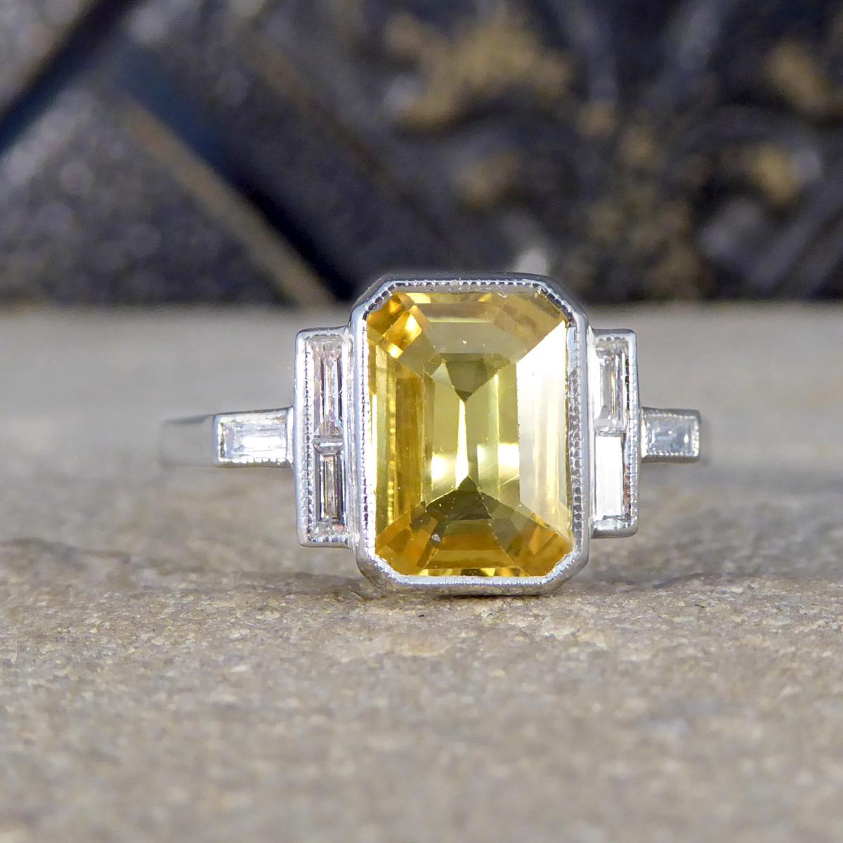 Embrace the allure of a bygone era with this exquisite Art Deco-inspired ring, a masterpiece of design and craftsmanship. This captivating piece features a striking yellow sapphire, complemented by baguette-cut diamonds accenting each shoulder, all