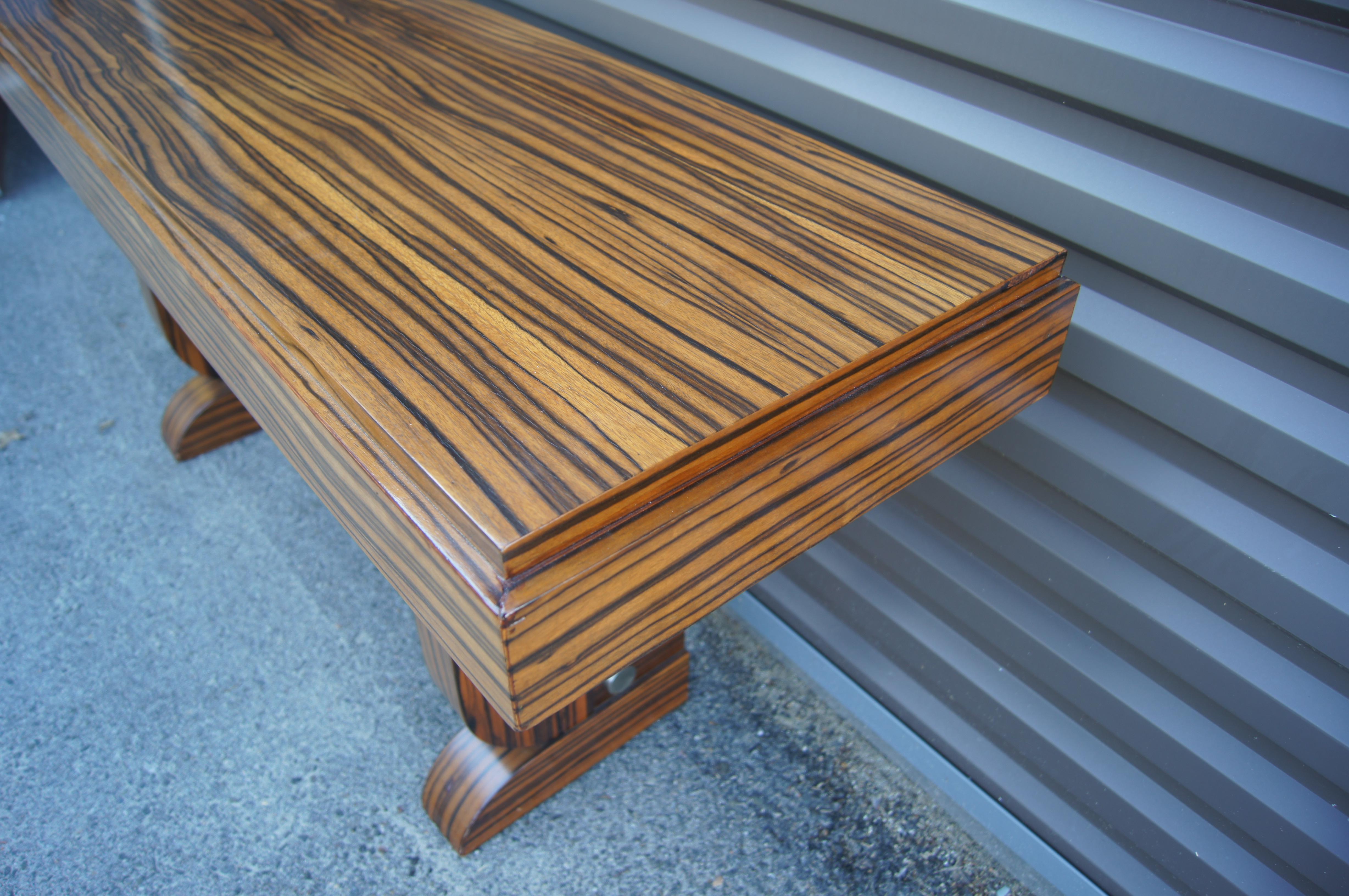 This striking console, in a richly grained zebrawood, has a muscular Art Deco aesthetic. The top is 4.5 inches thick with a slight setback along the front and sides. An aluminum bar stabilizes the 3-inch-thick legs, which curve inward and back out