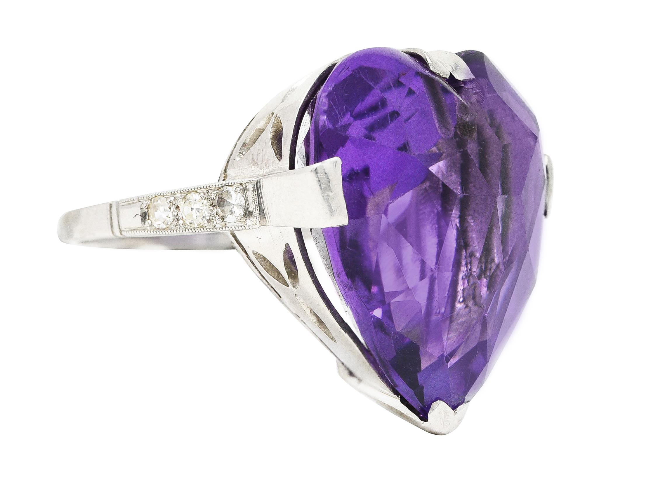 Centering a heart shaped rose cut amethyst measuring 20.0 x 20.0 mm. Transparent reddish-purple in color with medium saturation. Drilled and set with wide prongs in a pierced foliate basket. Flanked by cathedral shoulders bead set with single cut