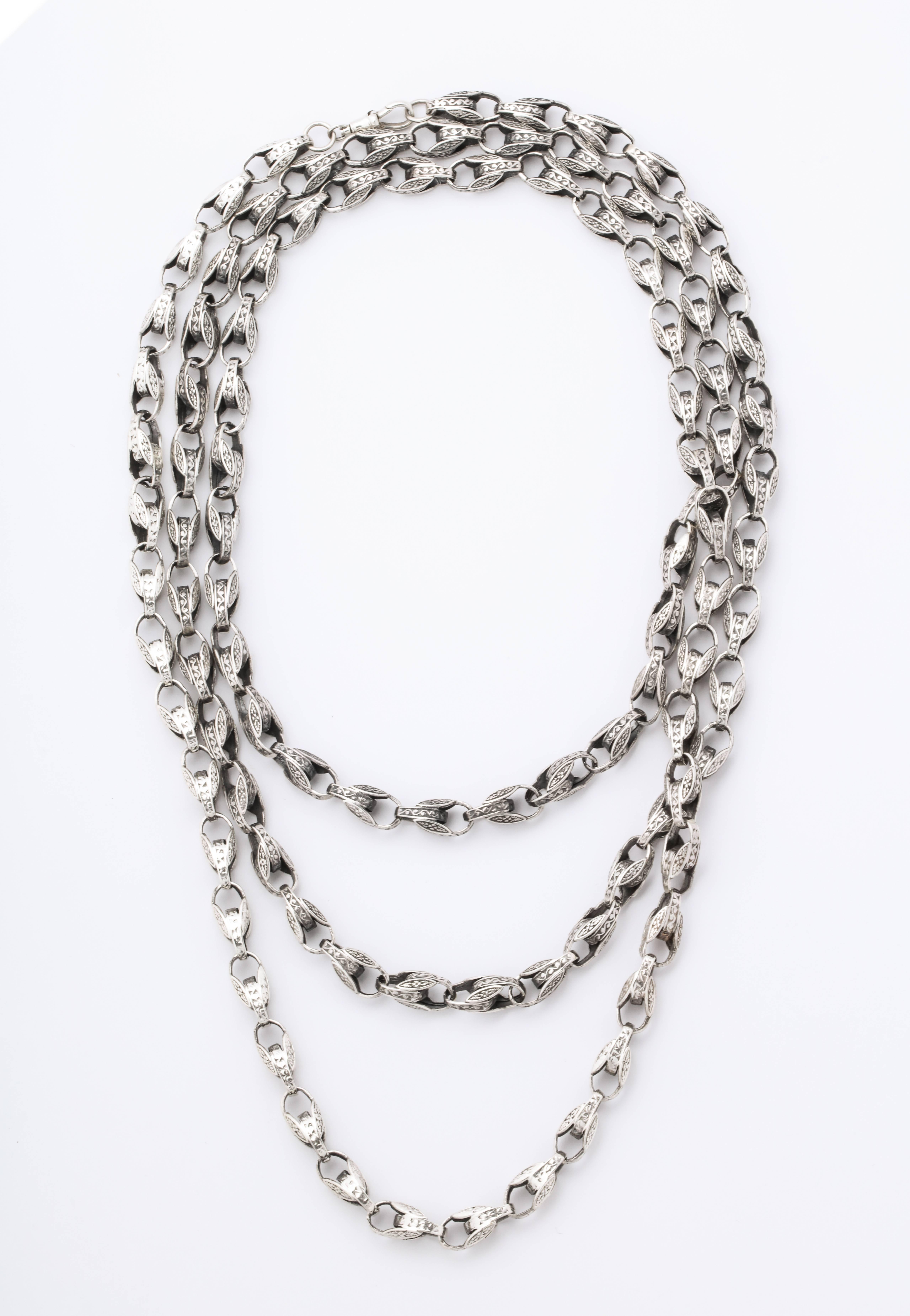 Substantial and eye catching, originating c. 1920-1930, this sterling silver long chain has completely engraved oval links connected in opposite directions. The links are 3/4 of an inch long and the opposing connections are 3/8 inch long. The chain